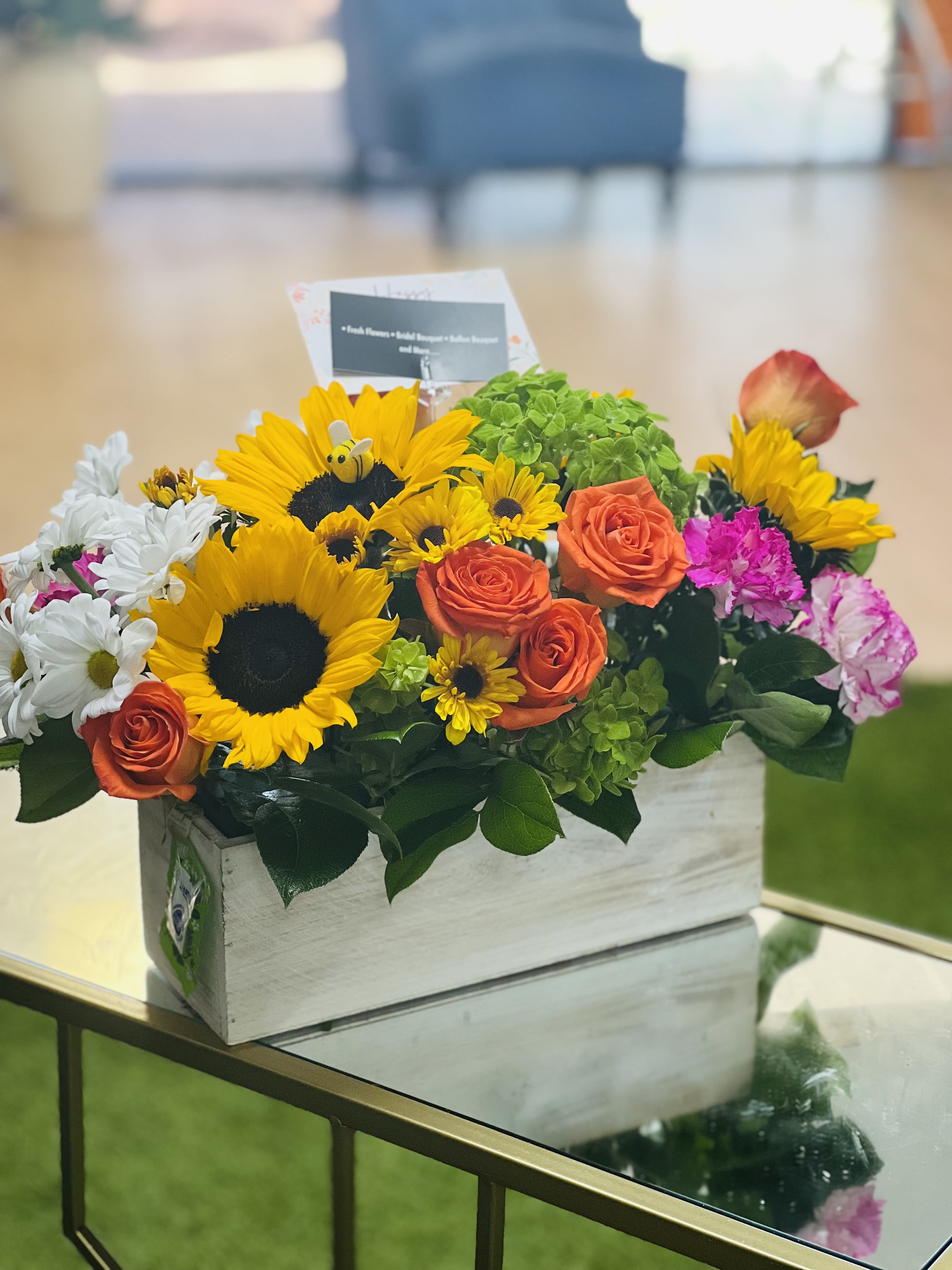 Mixed bouquet in a white wooden box with sunflowers, roses, and daisies