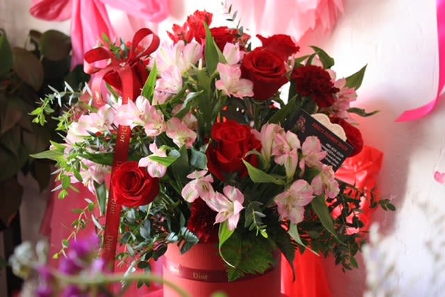 Red roses and pink lilies arranged in a red box with ribbon