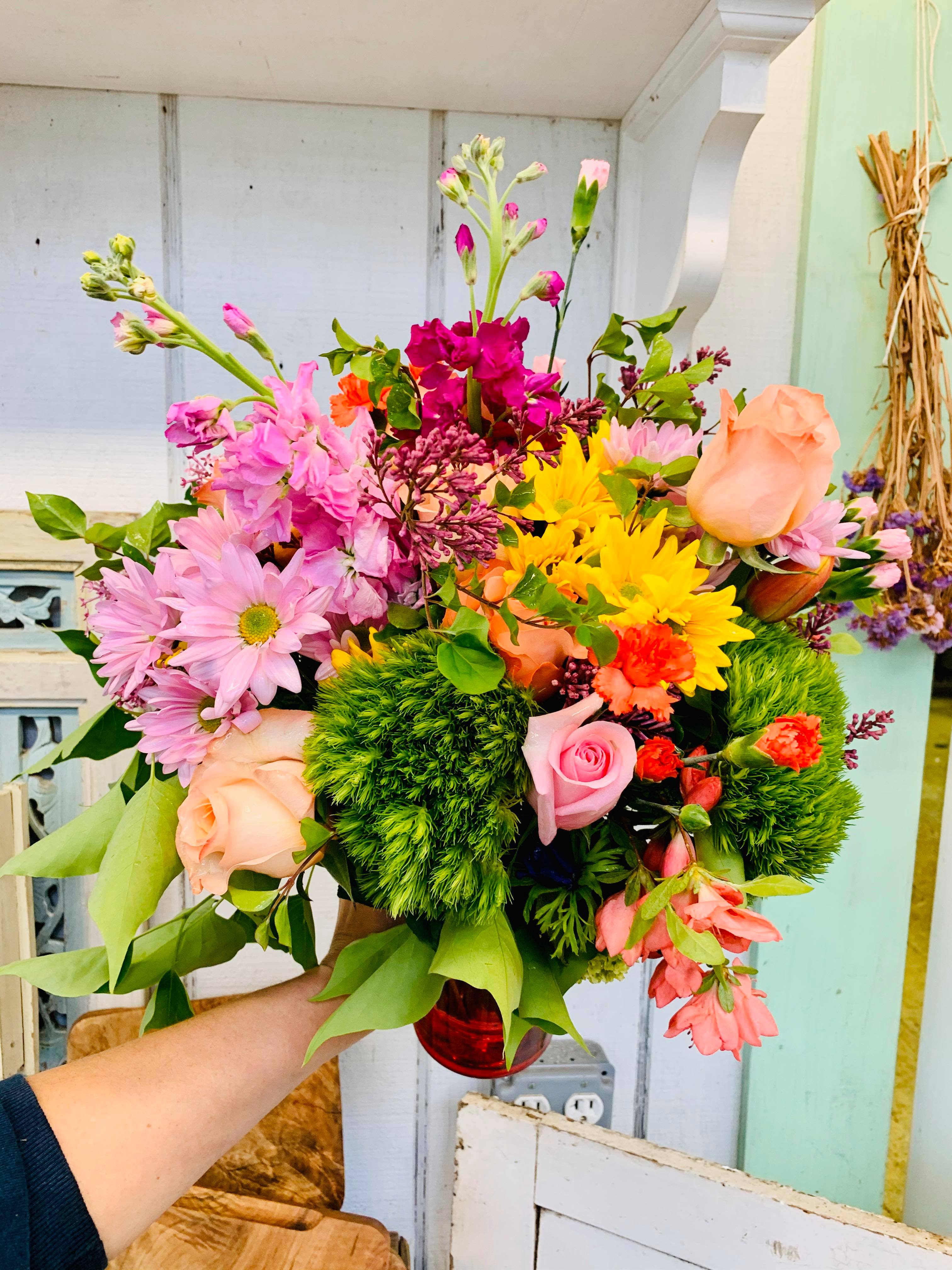 Mixed bouquet of pink, peach, and yellow flowers in a red vase
