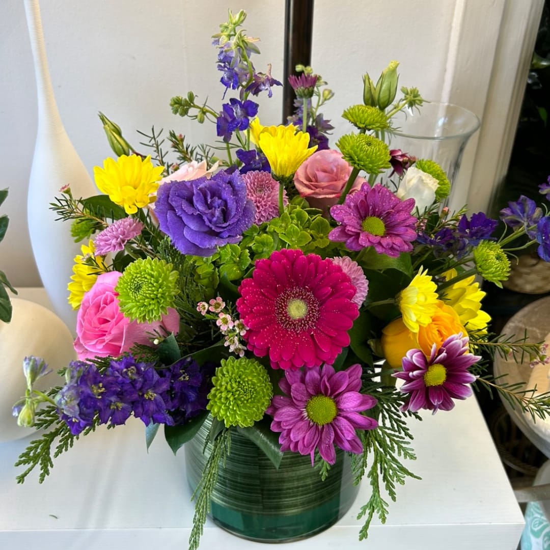 Colorful mixed bouquet in a green glass vase with purple, pink, and yellow blooms