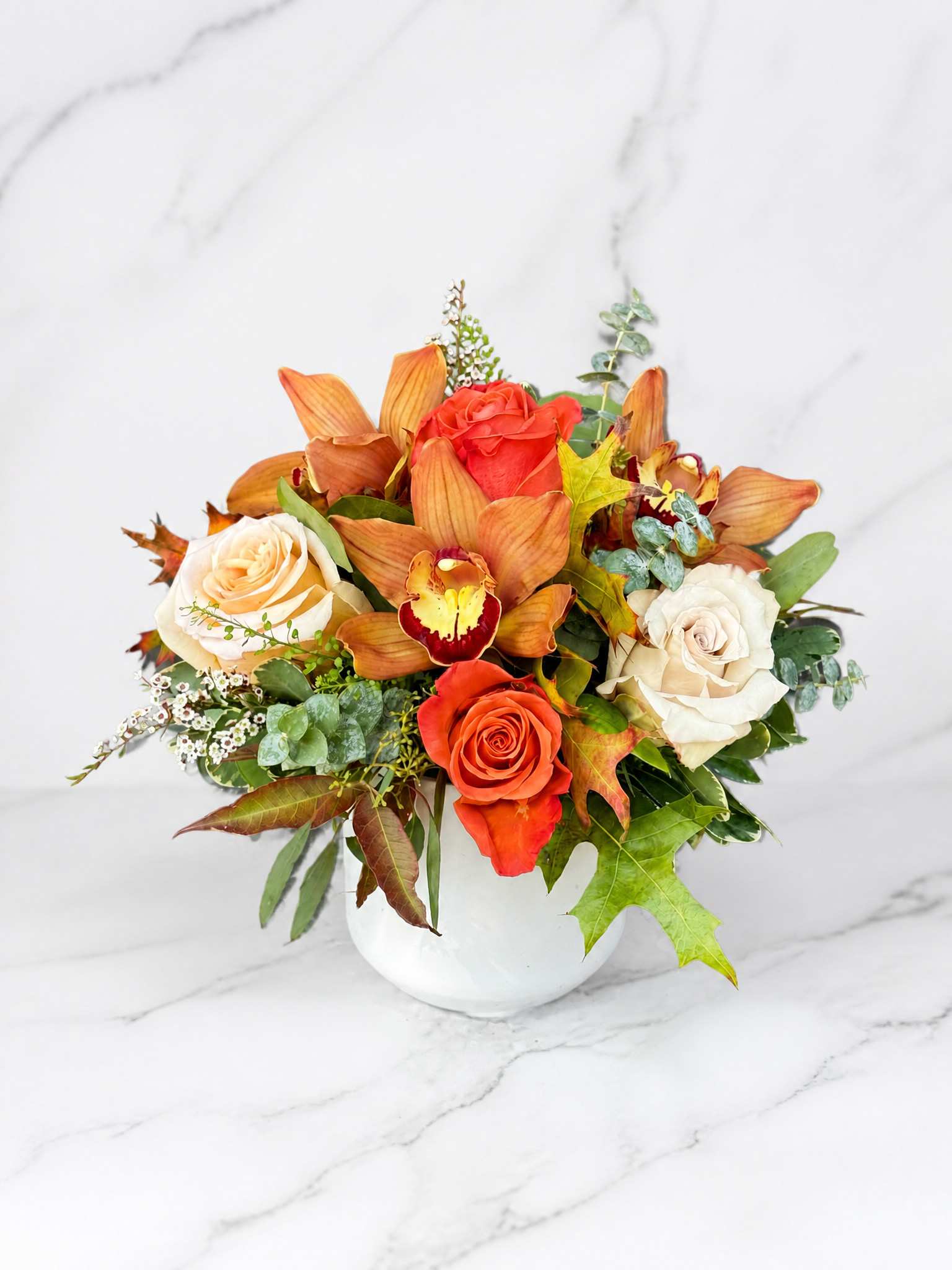 Orange and white roses with orchids in a white vase