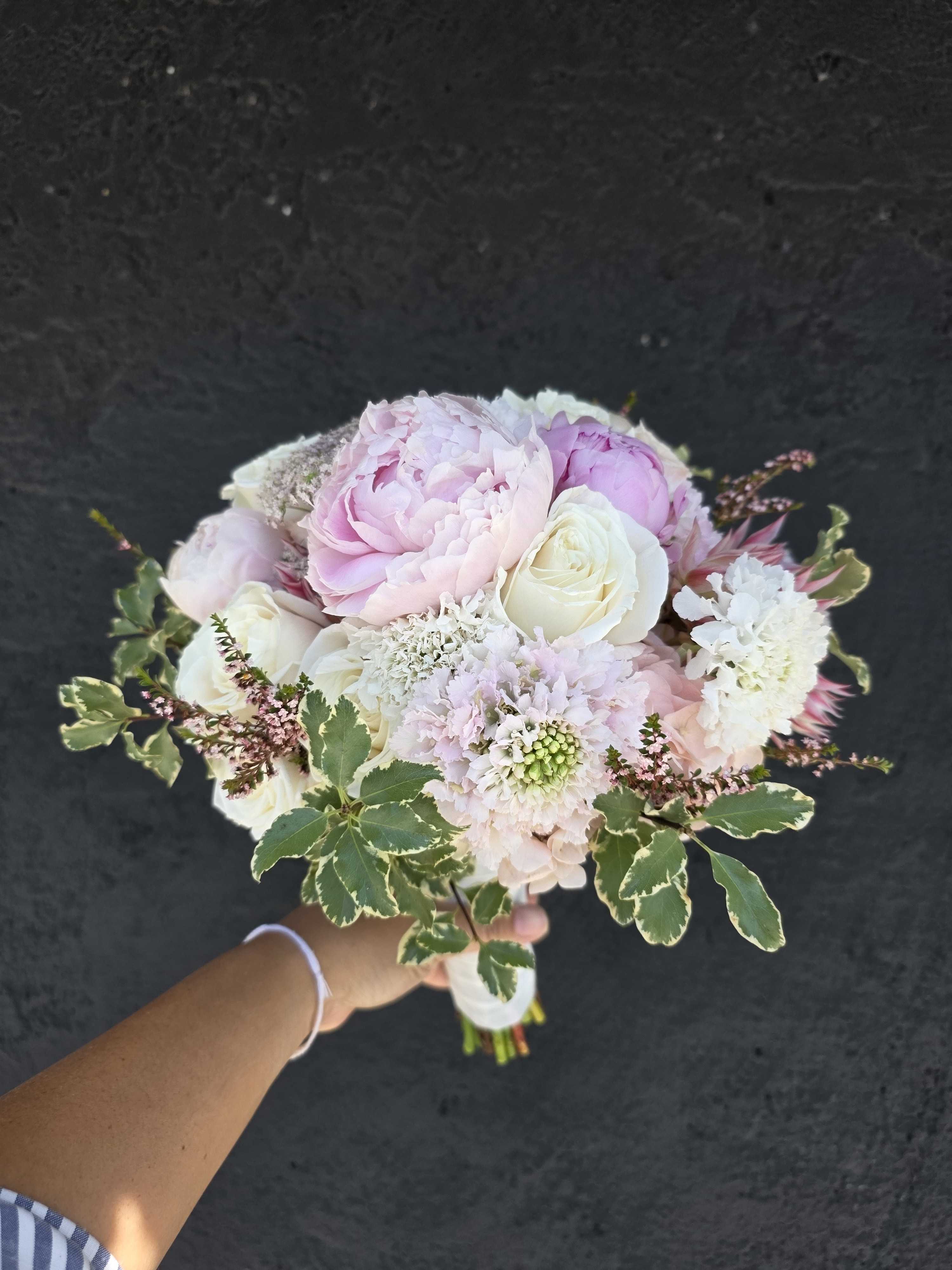 Handheld bouquet of pale pink and white flowers with variegated greenery