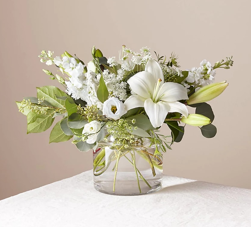 White lilies and mixed white flowers in a clear glass vase