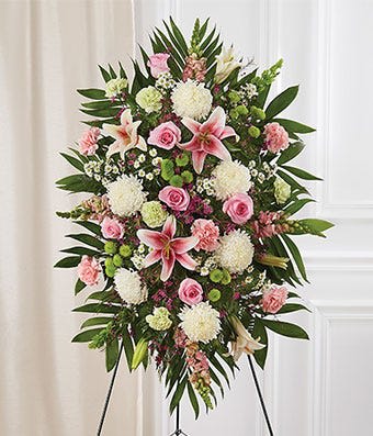 Standing floral spray with pink lilies, roses, and white blooms on an easel