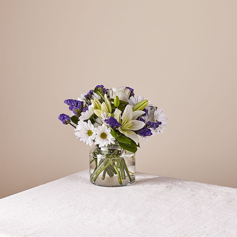 White lilies and daisies in a clear glass vase with purple filler flowers