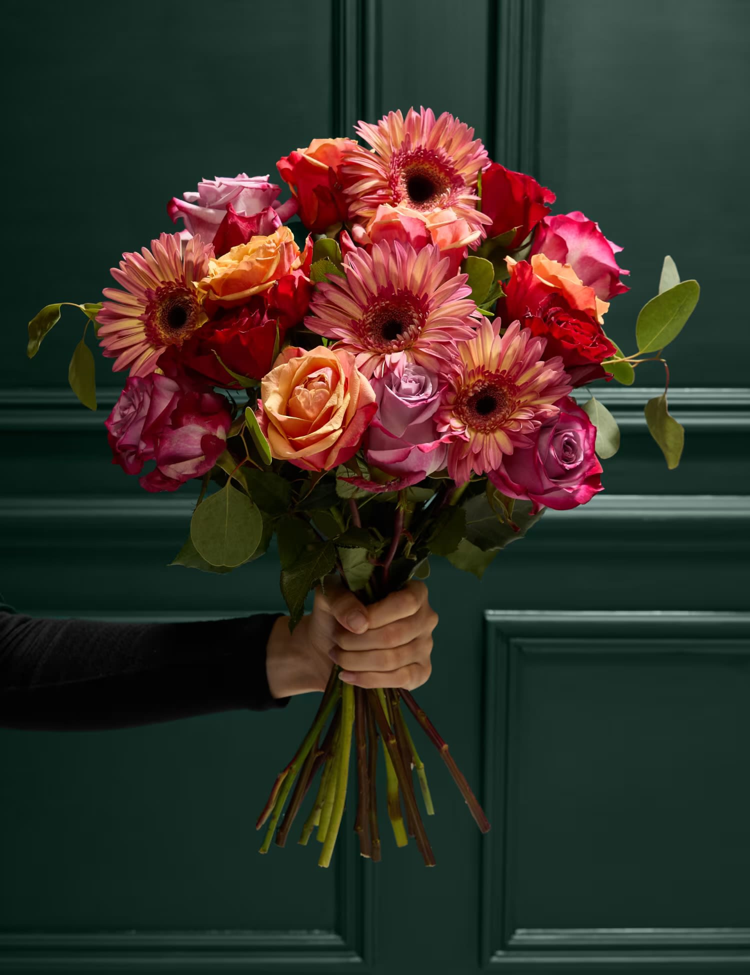 Handheld bouquet of pink and orange roses with gerbera daisies