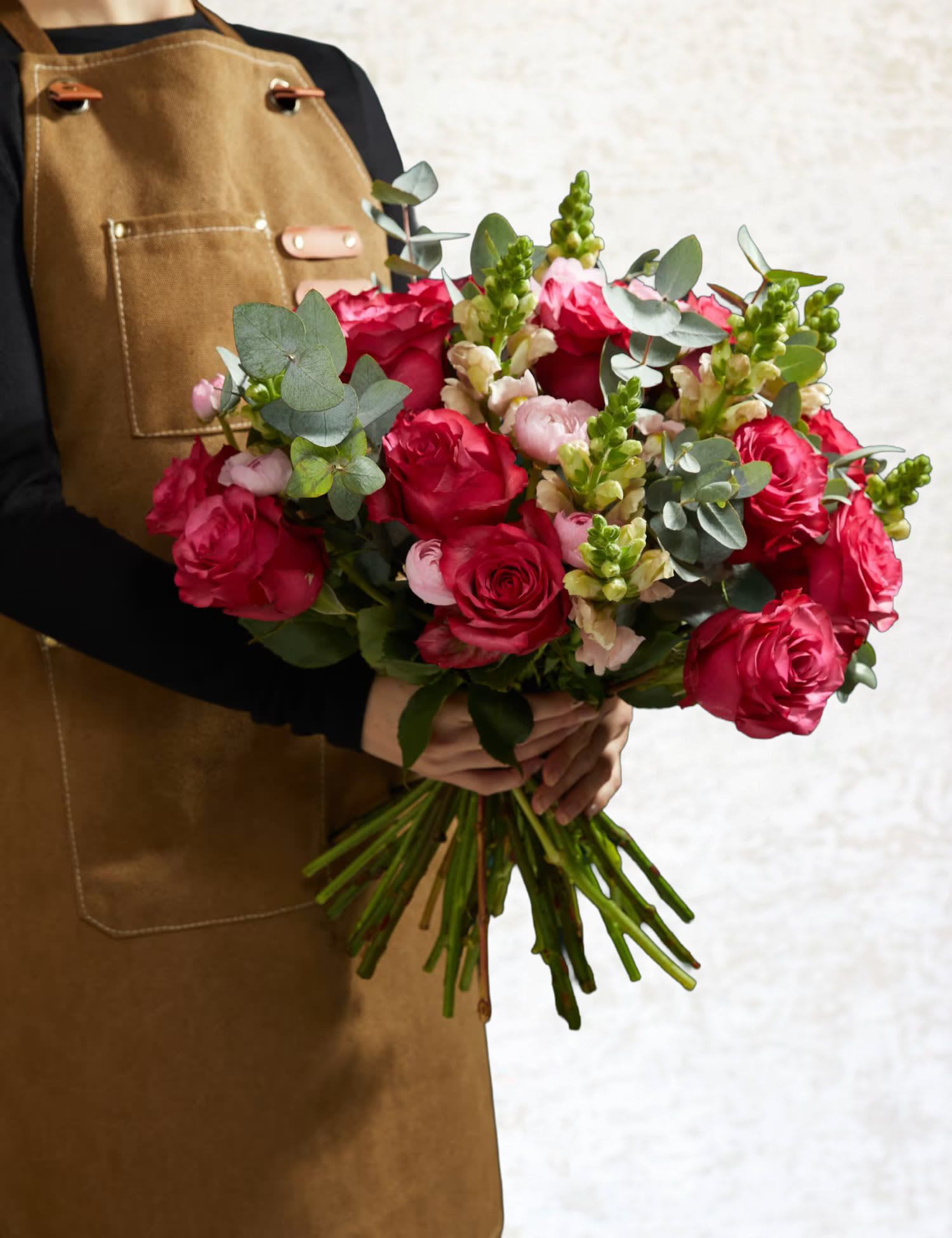 Handheld bouquet of red roses with pink blooms and eucalyptus