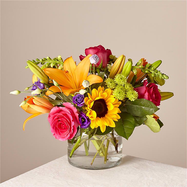 Mixed bouquet of roses, lilies, and a sunflower in a glass vase