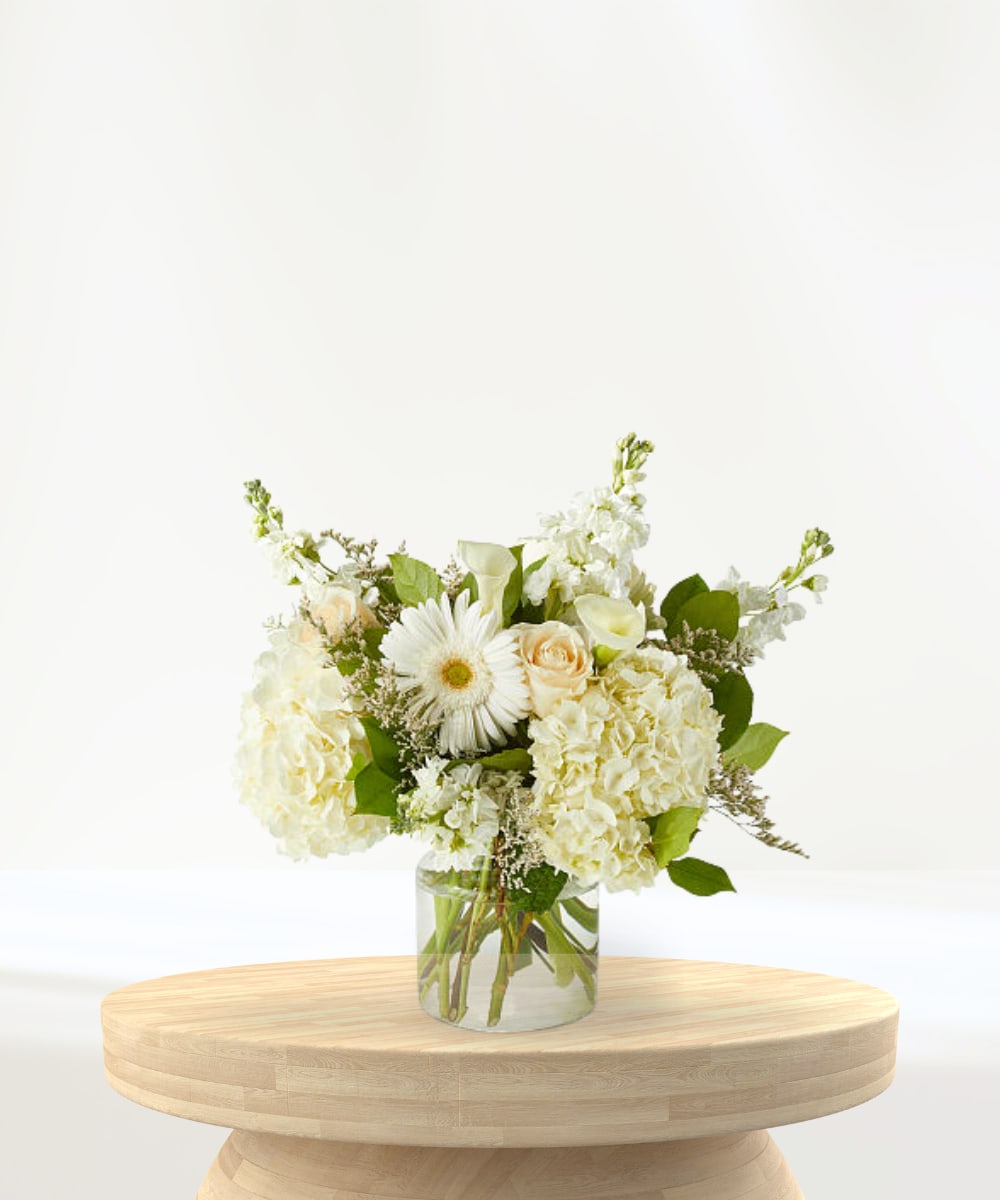 White floral arrangement in a clear glass vase on a wooden table