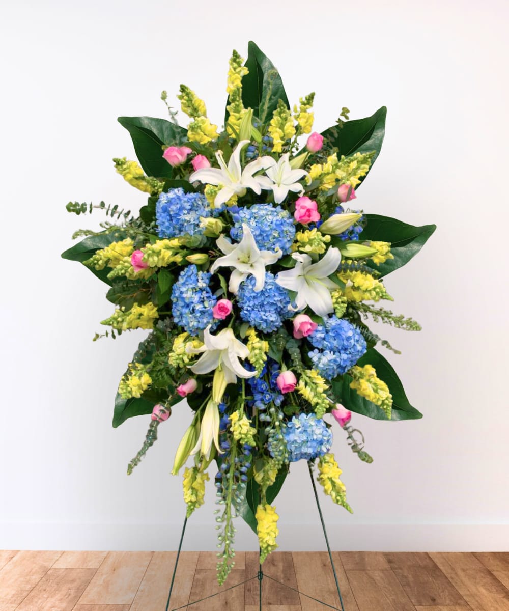 Standing floral spray with blue hydrangeas, white lilies, and yellow snapdragons