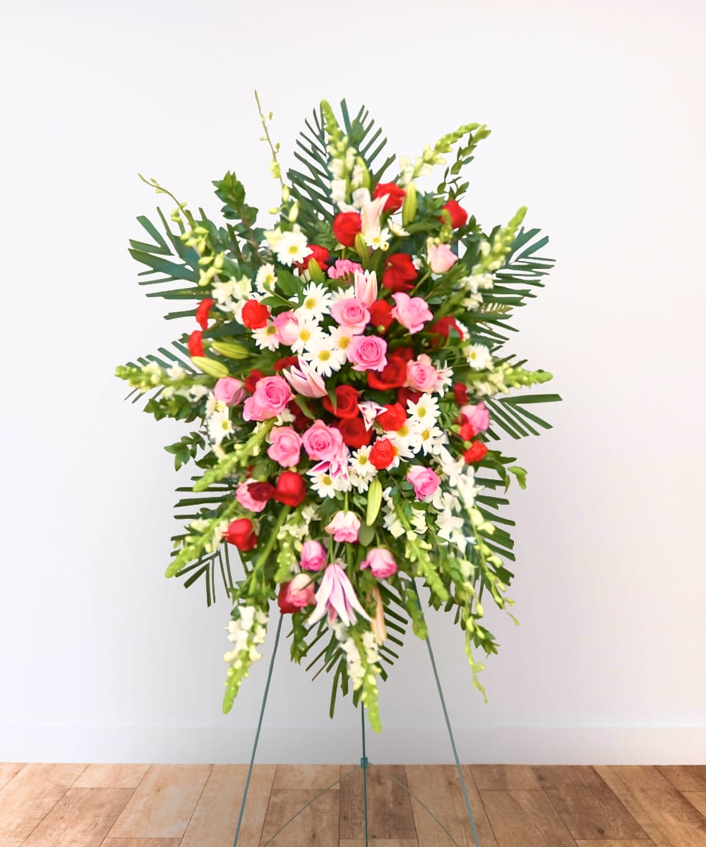 Standing floral spray with pink and red roses, white daisies, and tropical leaves