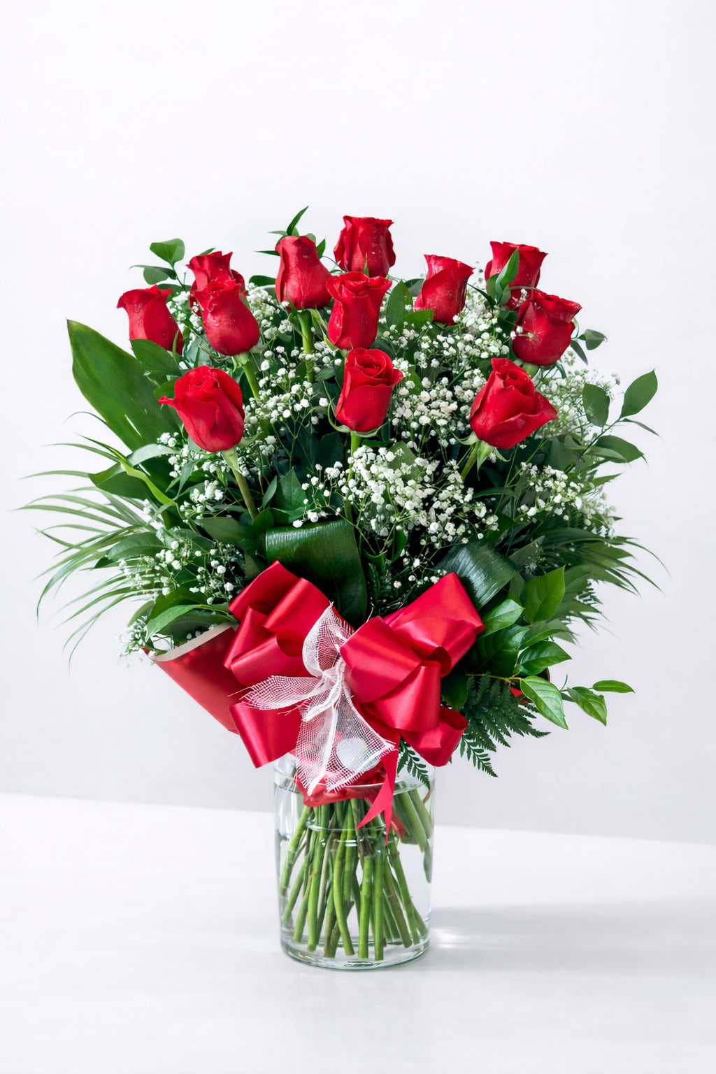 Red roses arranged in a clear glass vase with a red ribbon bow