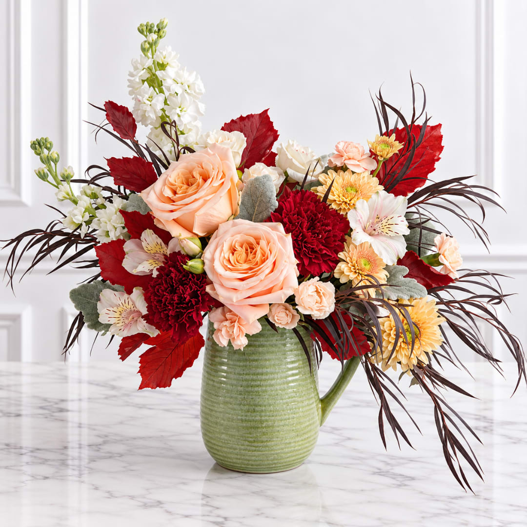Peach roses and mixed flowers in a green ceramic pitcher vase