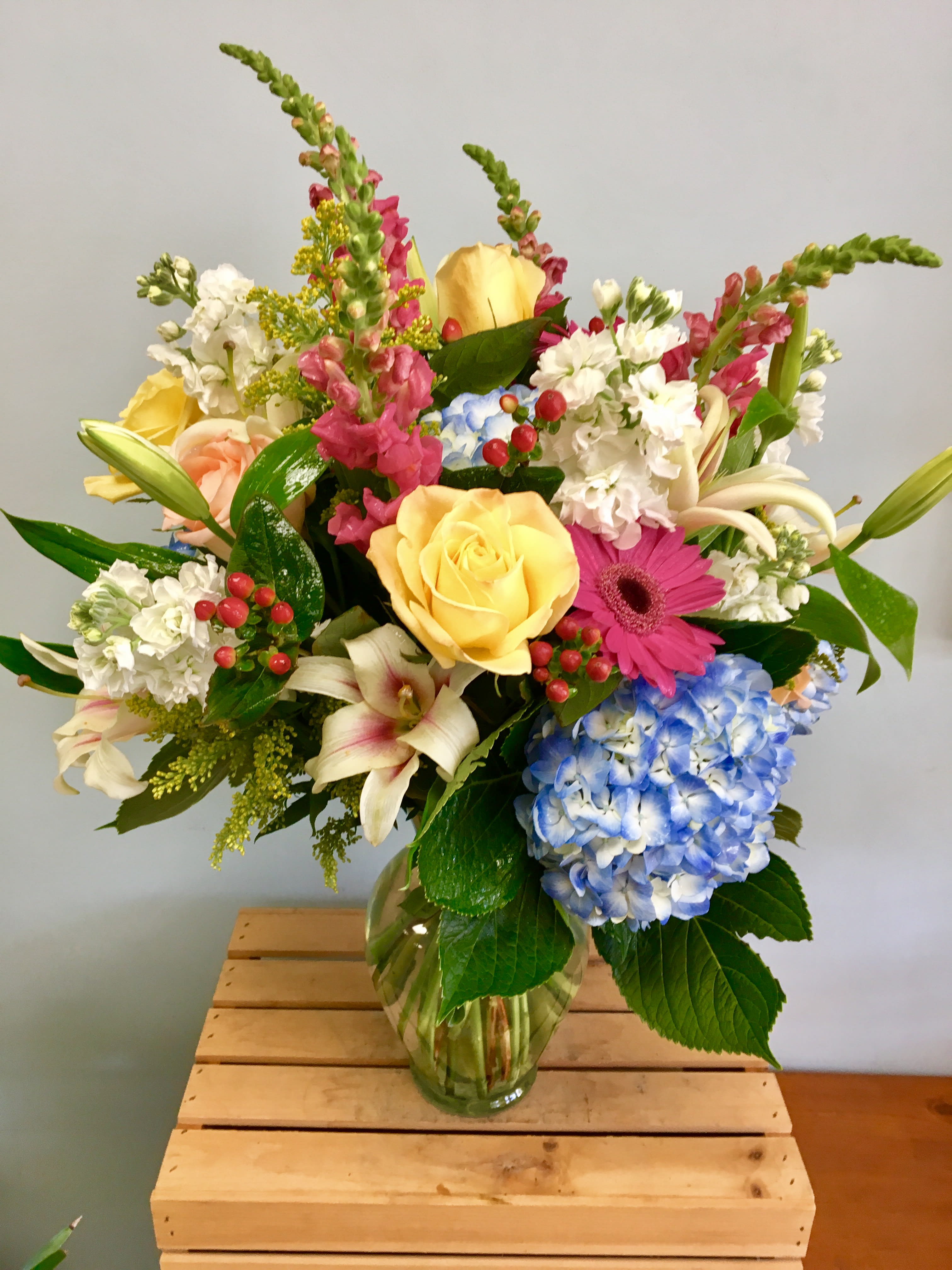 Mixed bouquet of roses, hydrangea, lilies, and gerbera daisies in a glass vase
