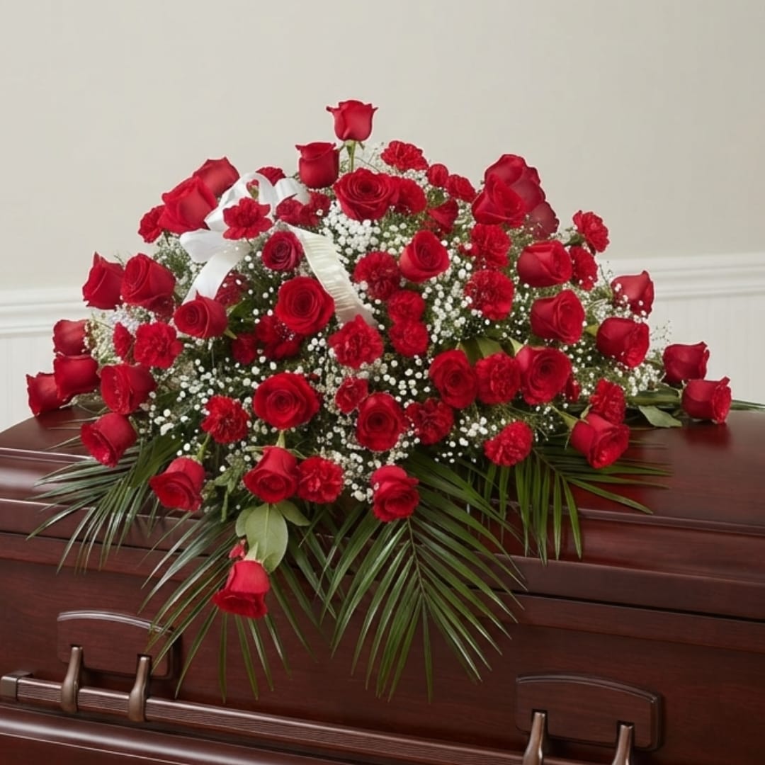 Red rose and carnation arrangement on a casket with white ribbon