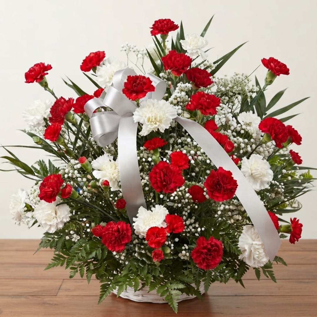Red and white carnation arrangement in a white basket with a silver ribbon