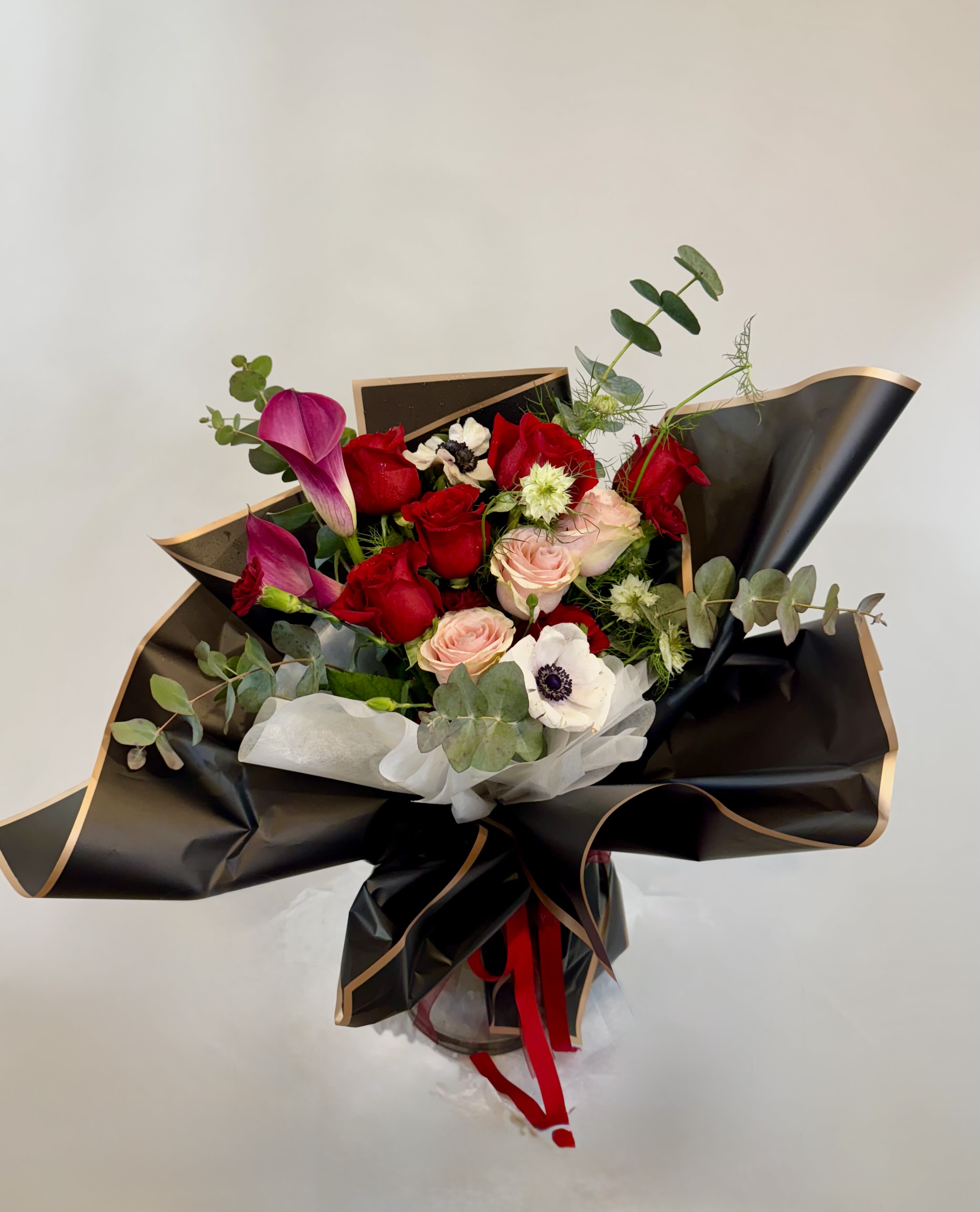 Bouquet of red and pink roses with purple calla lilies in black wrap