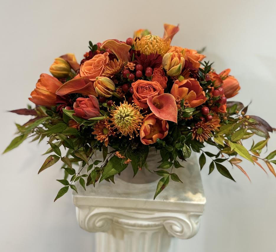 Orange floral arrangement in a white pedestal vase