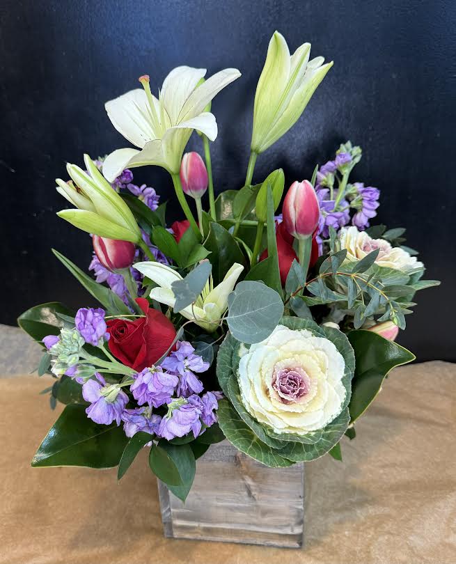 Mixed bouquet with lilies, roses, and purple blooms in a clear square vase