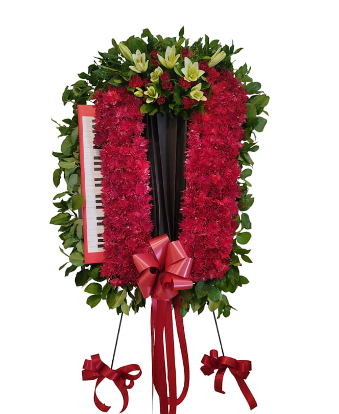 Standing floral wreath with red flowers, lilies, and a piano inset