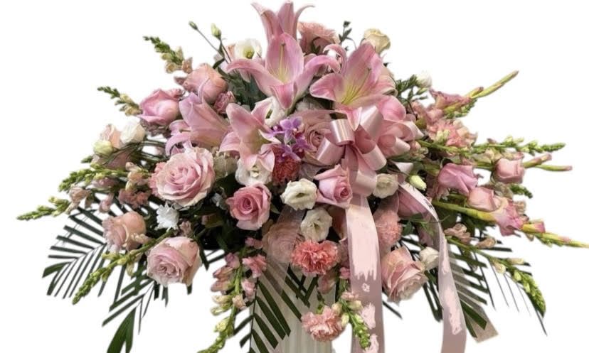 Pink floral spray with roses and lilies, accented by a pink ribbon