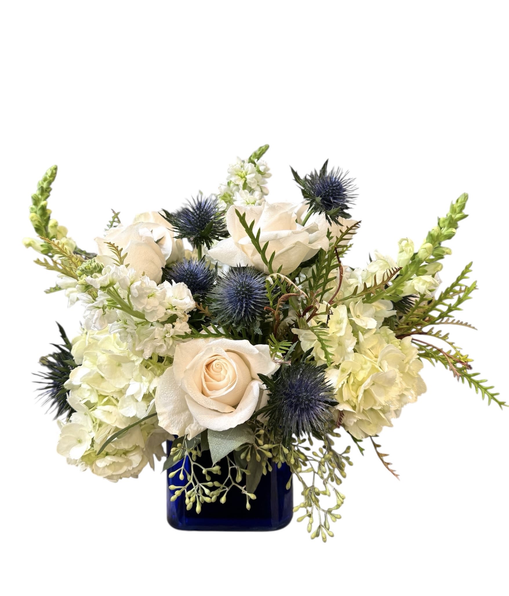 White roses and pale blooms in a blue vase with spiky blue thistles
