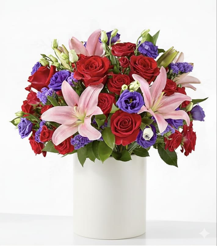 Bouquet of red roses, pink lilies, and purple blooms in a white vase