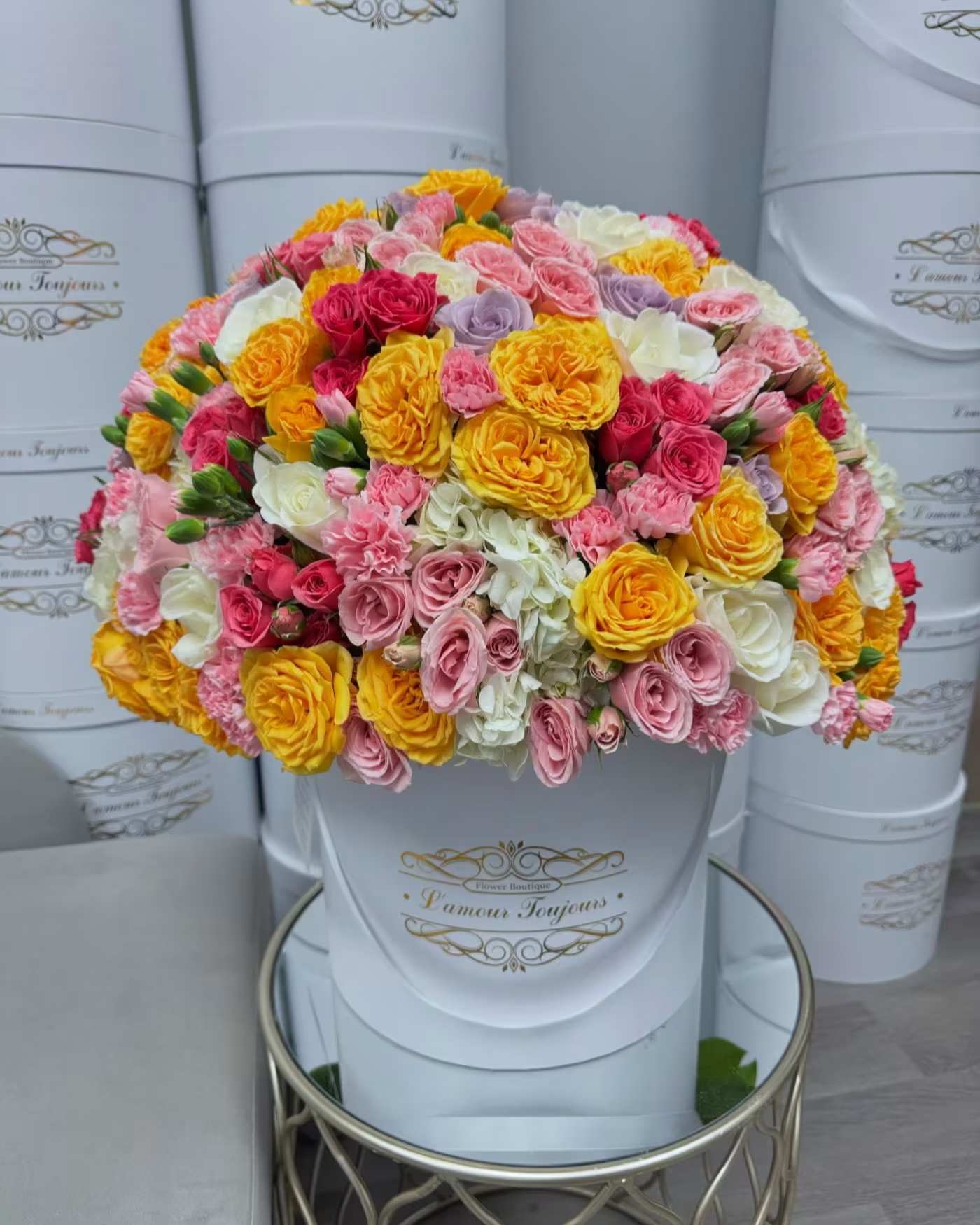 Round bouquet of pink, yellow, white, and lavender roses in a white hat box