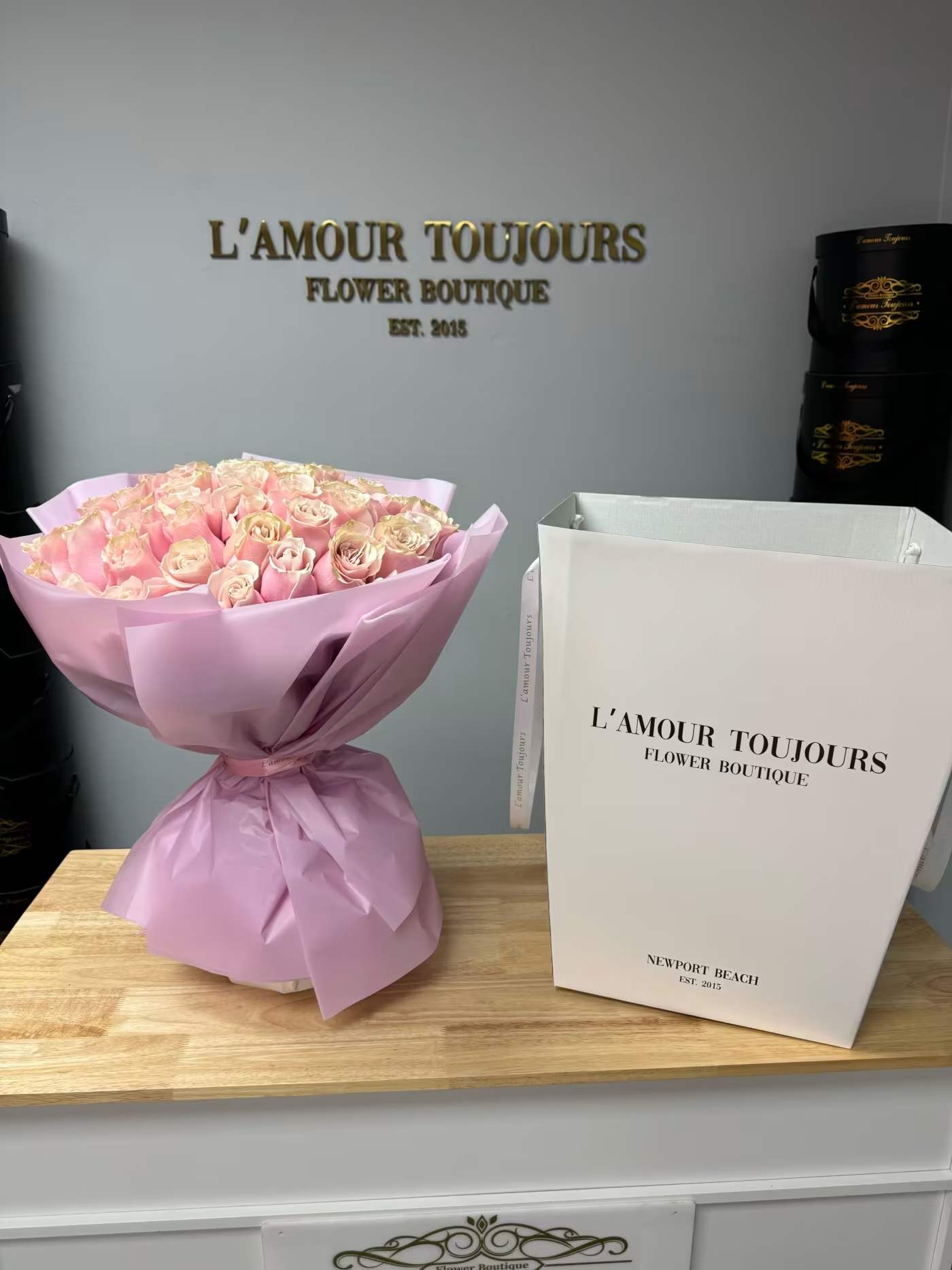 Bouquet of pale pink roses wrapped in lavender paper beside a white gift bag