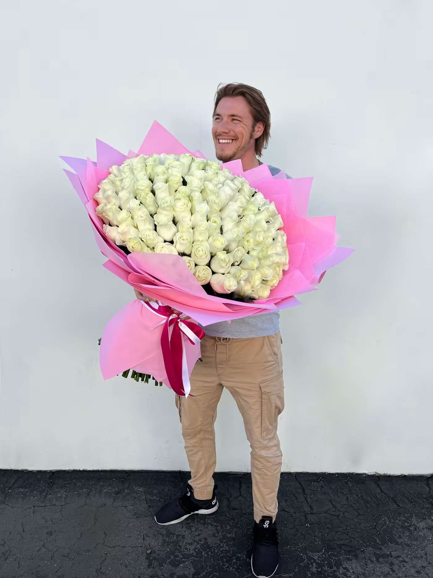 Man holding a large bouquet of white roses wrapped in pink paper