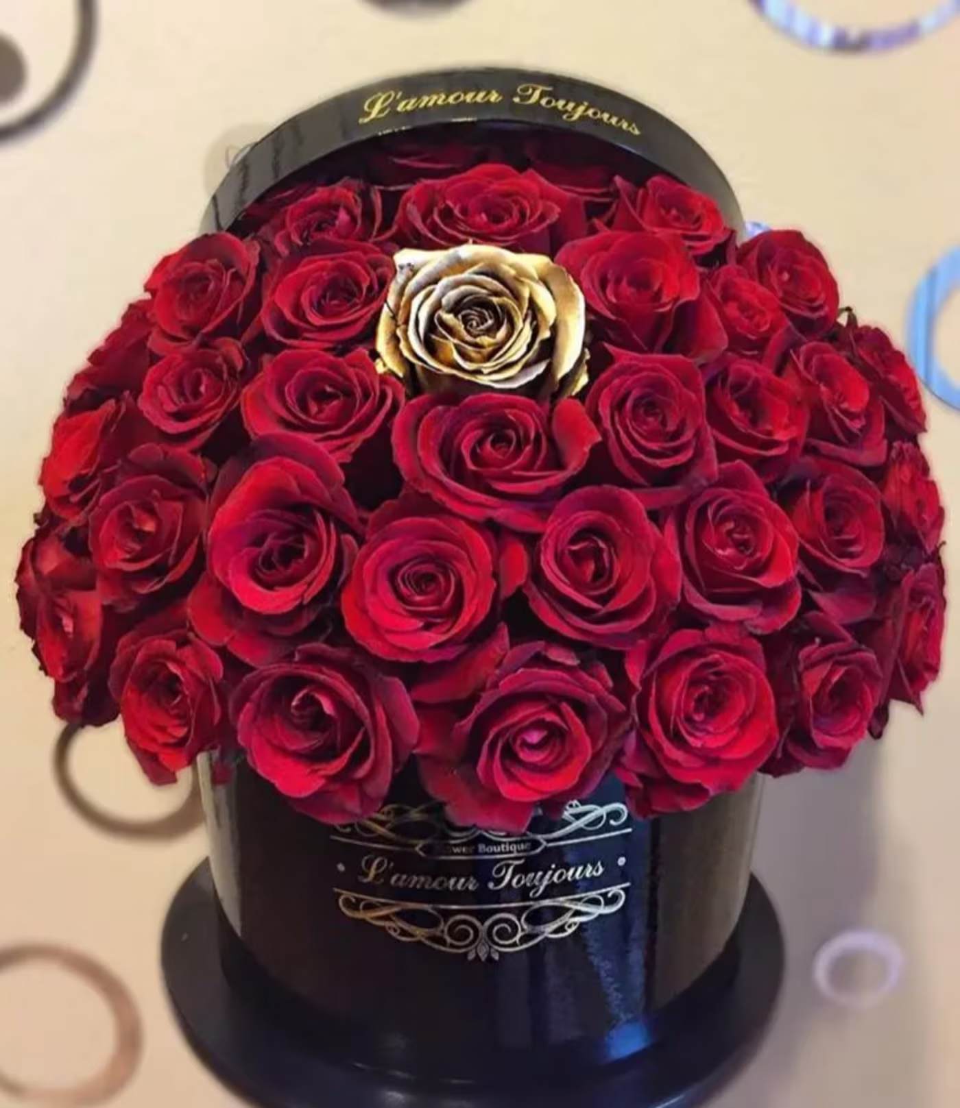 Round box of red roses with one gold rose in the center