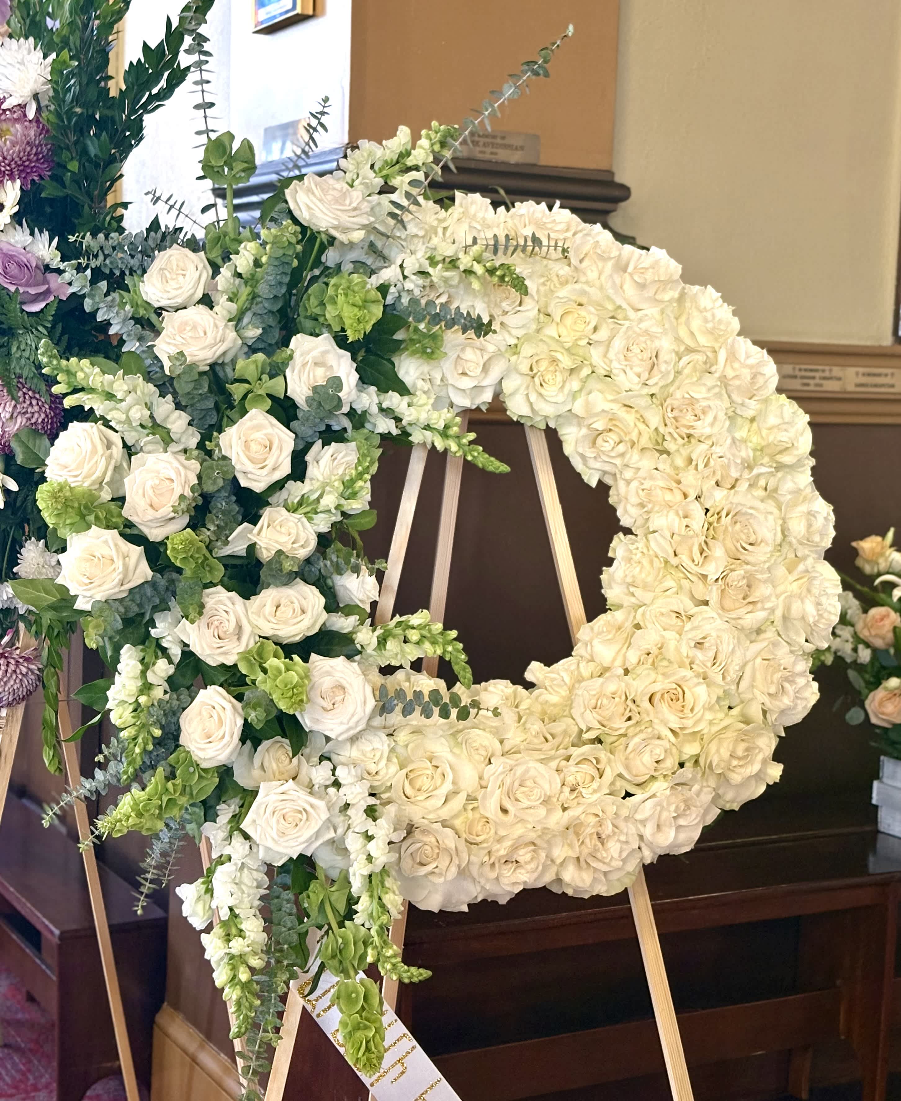 Large floral wreath of white roses and green accents on an easel.