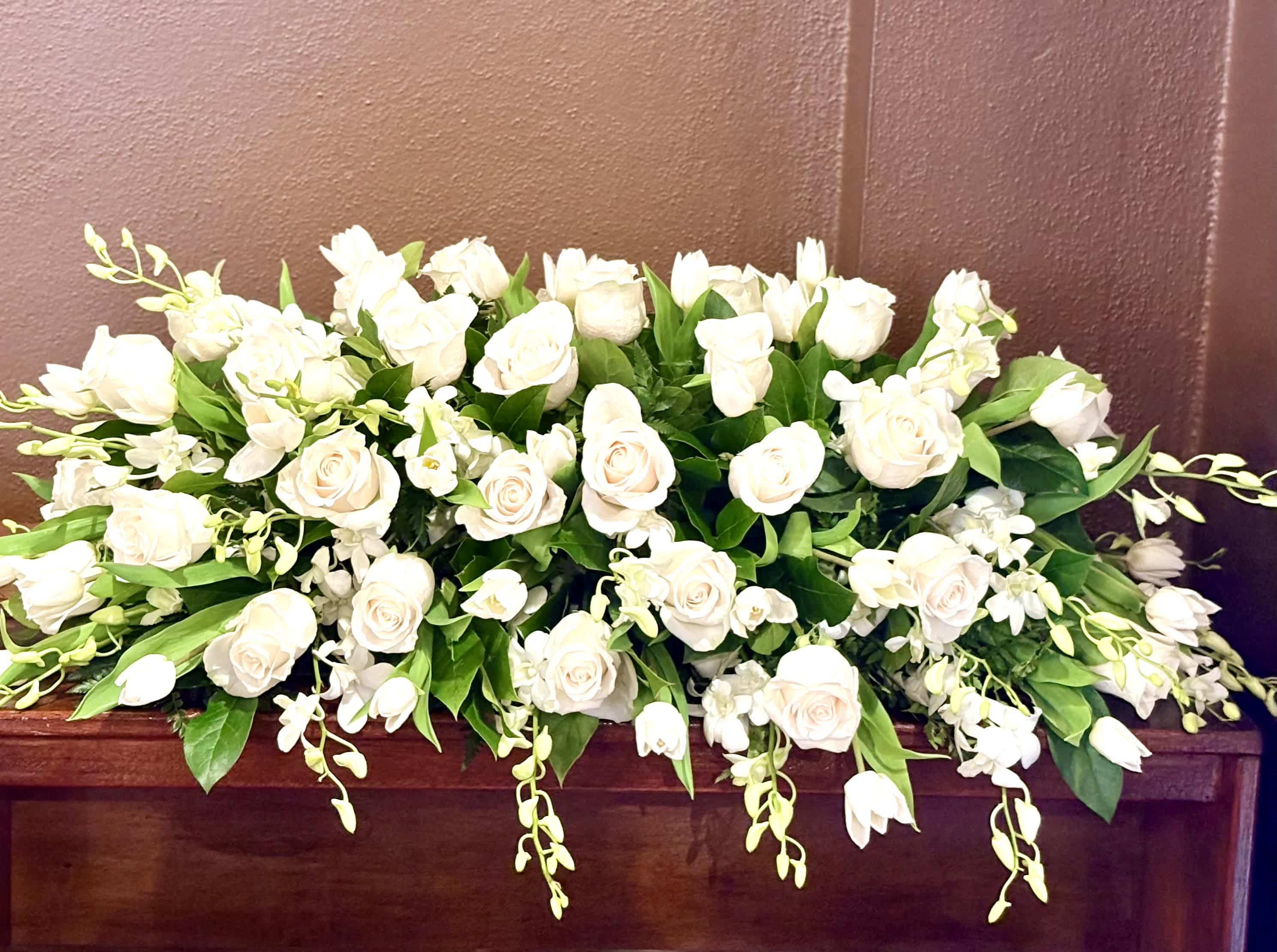 Low arrangement of white roses and orchids on a wooden surface