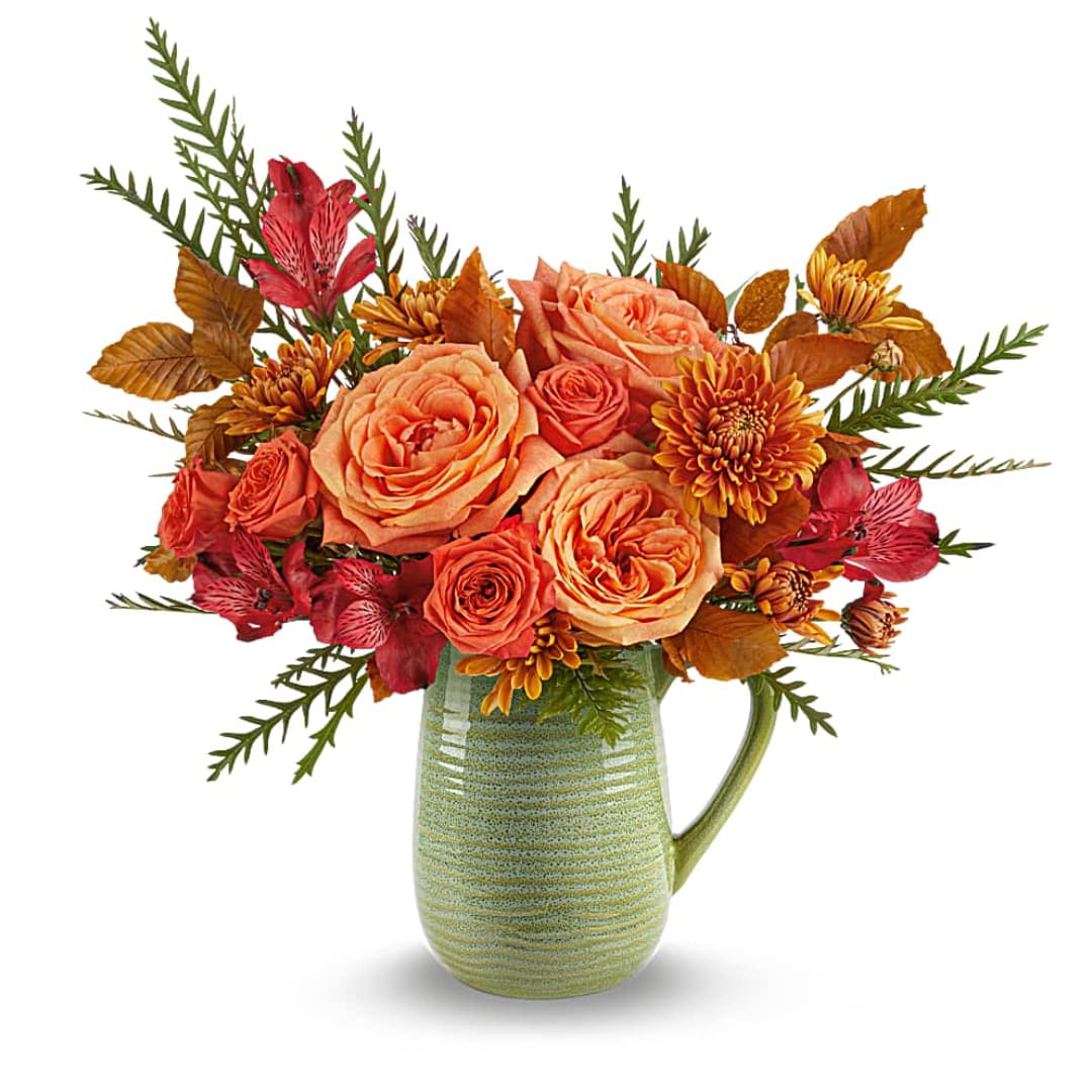 Orange roses and red flowers arranged in a green ceramic pitcher