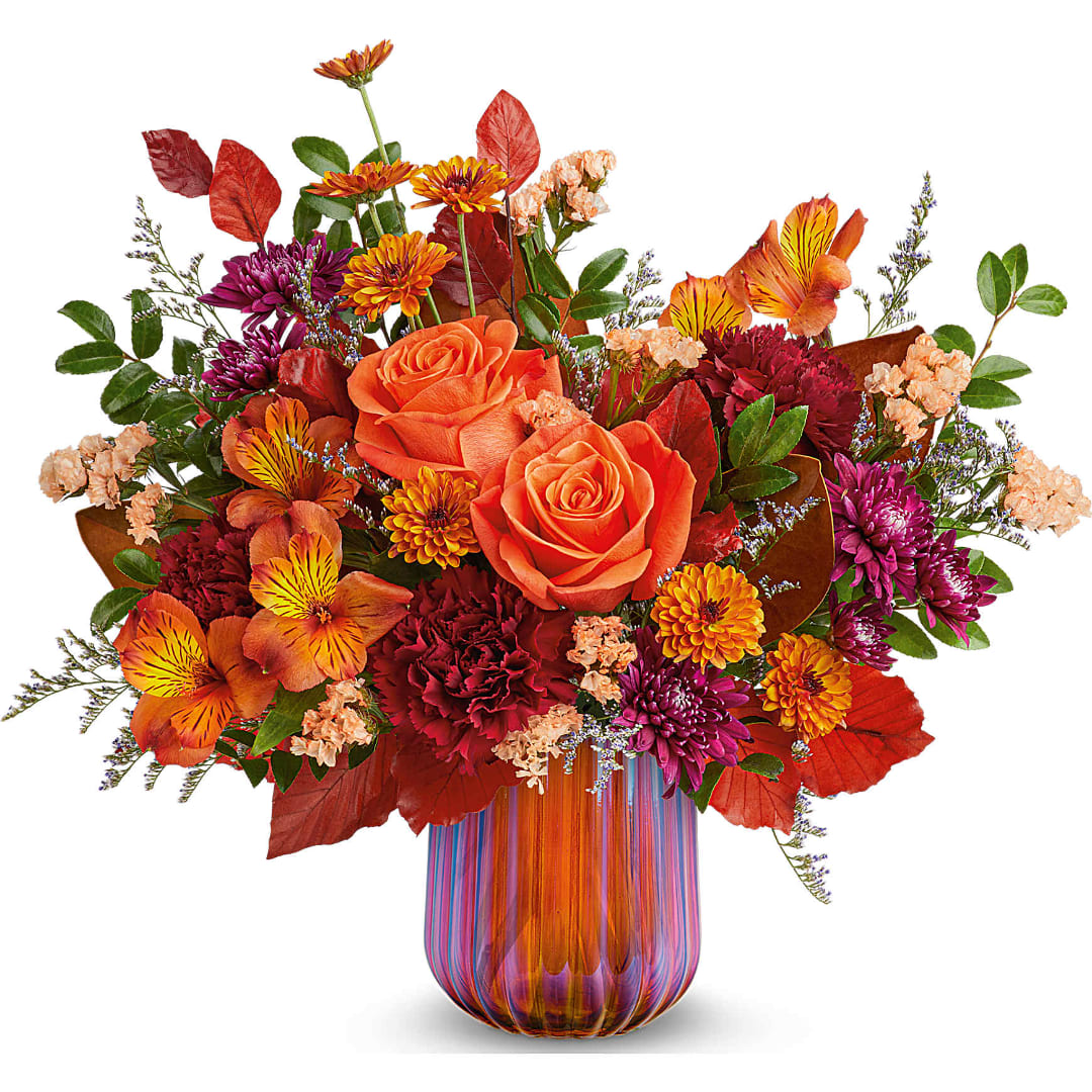 Orange roses and mixed fall flowers in a striped glass vase