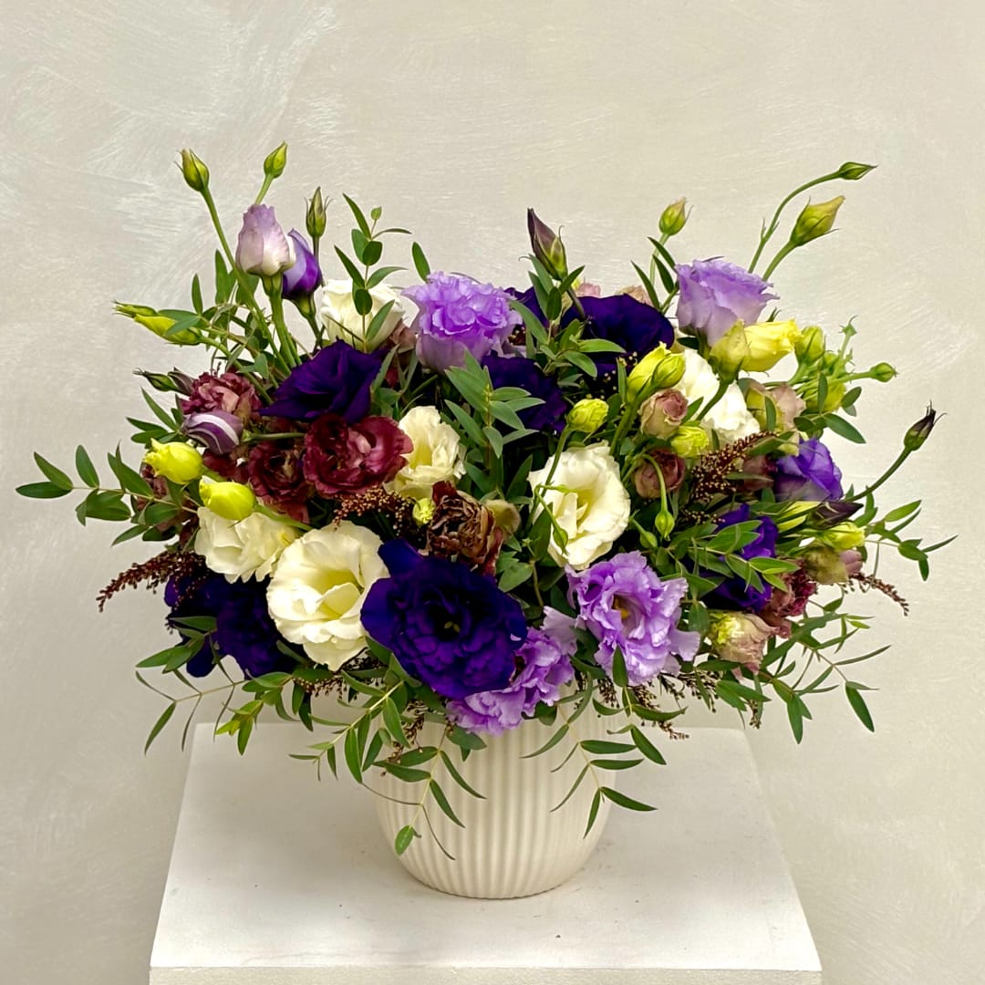 Purple, white, and yellow flowers in a ribbed white vase