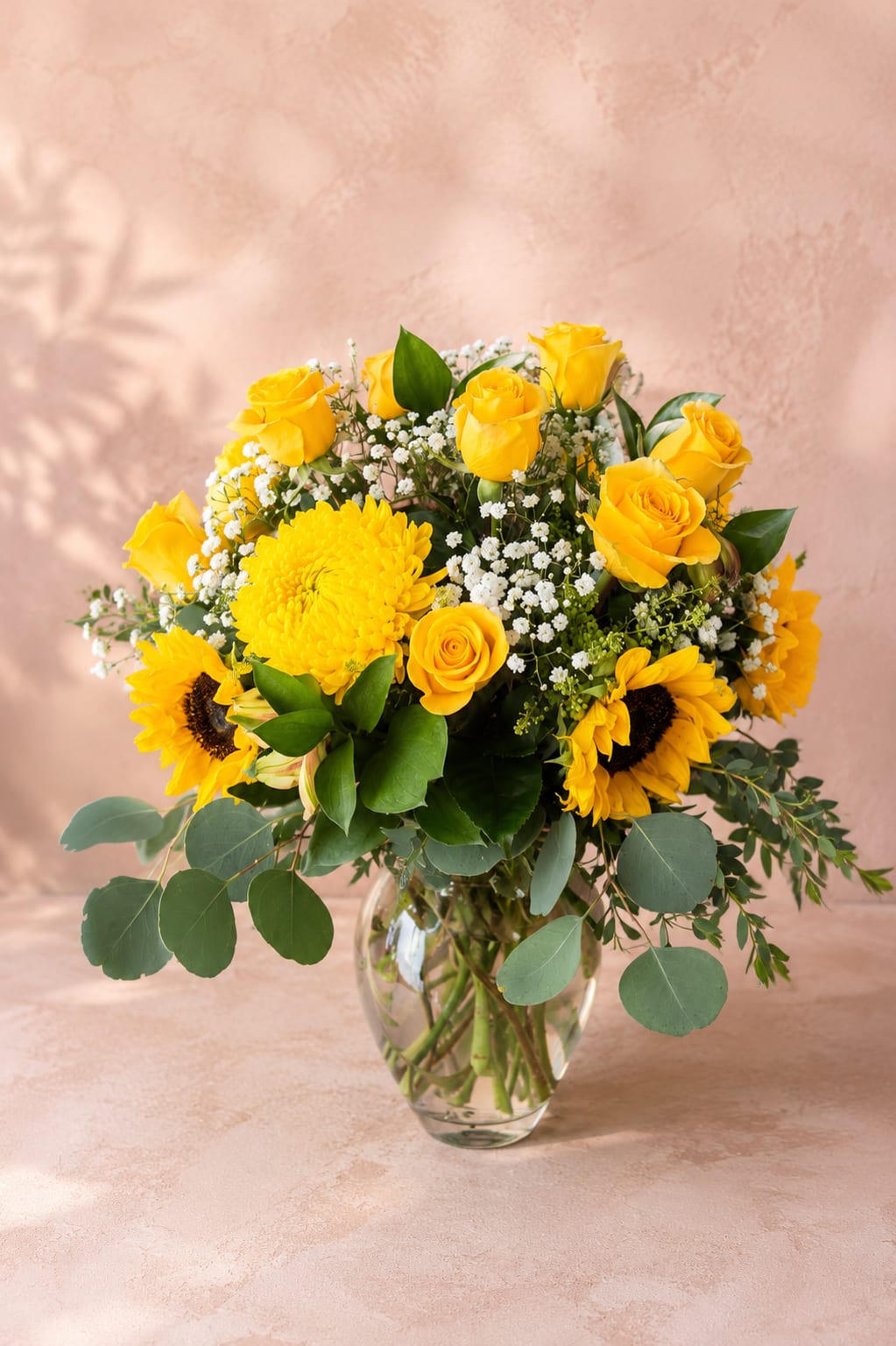 Amaterasu's Golden Radiance – Luxury Vase - Inspired by Amaterasu, the Japanese goddess of the sun and light, this joyful arrangement celebrates warmth, happiness, and new beginnings.  Amaterasu's Golden Radiance combines cheerful sunflowers with sunny yellow roses, a vibrant yellow football chrysanthemum, delicate baby's breath, and fresh seasonal greenery in a clear glass vase. Rich golden tones and lush textures create an uplifting design that instantly brightens any room.  Perfect for birthdays, congratulations, thank-you gifts, housewarmings, get-well wishes, or simply bringing sunshine to someone's day, this handcrafted arrangement is full of warmth and positive energy.  Each arrangement is created by Flower Fairy using the freshest premium flowers available. Seasonal substitutions may occasionally be necessary while preserving the overall color palette, style, and luxurious presentation.  Features: Premium sunflowers Yellow roses Yellow football chrysanthemum Baby's breath Fresh seasonal greenery Clear glass vase Handcrafted by Flower Fairy Same-day flower delivery throughout the Phoenix Metro Area