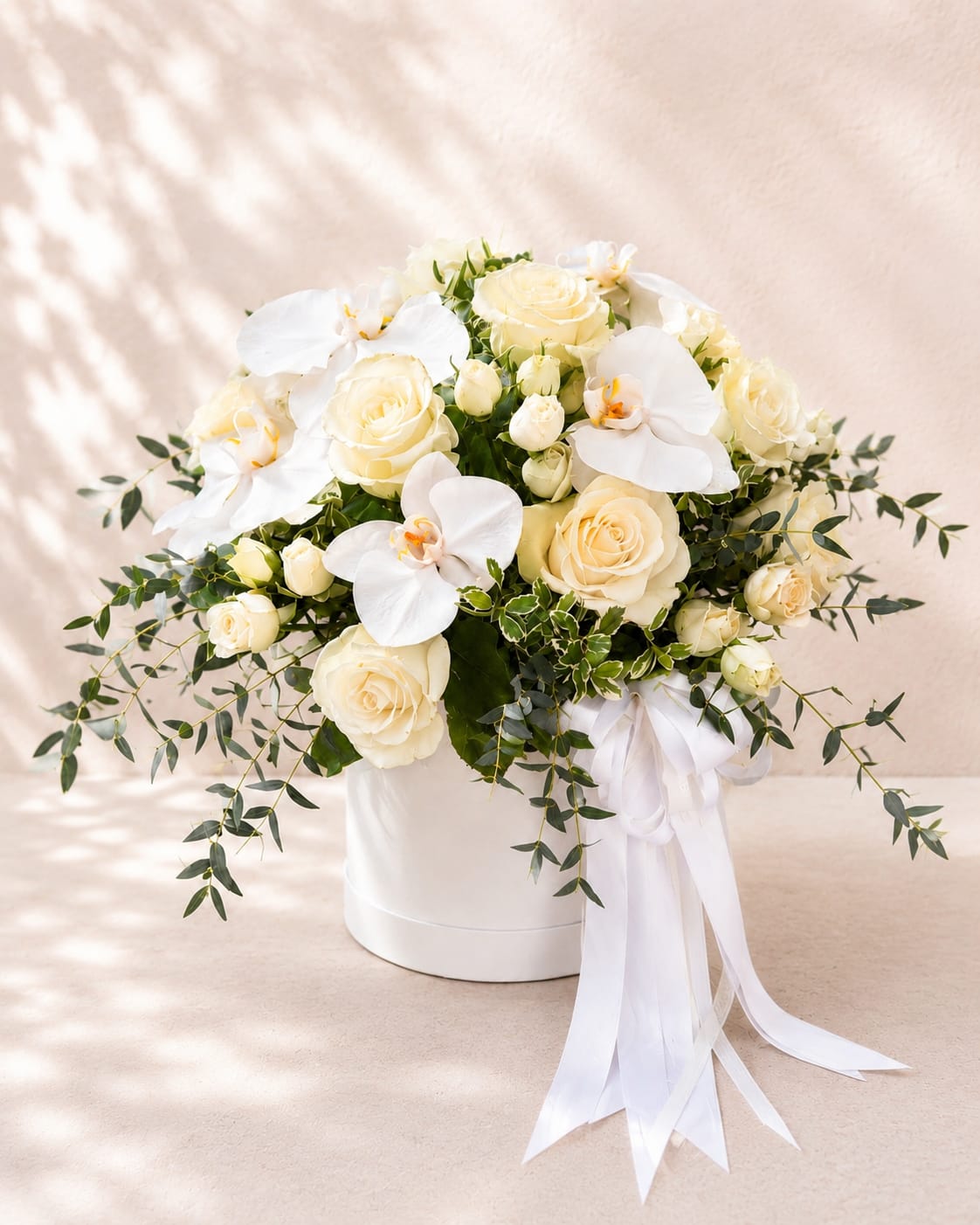 Hera's Eternal Grace - Luxury White Roses &amp; Orchids Box Arrangement - Inspired by Hera, the Greek queen of the gods and goddess of marriage, Hera's Eternal Grace embodies timeless elegance, devotion, and refined beauty.  This luxurious arrangement showcases premium white roses, delicate white spray roses, elegant orchids, and fresh greenery in Flower Fairy's signature white hat box. The graceful combination of velvety roses and cascading orchid blooms creates a sophisticated design that radiates purity, romance, and modern luxury.  Perfect for weddings, anniversaries, milestone celebrations, sympathy, housewarmings, or any occasion that calls for an unforgettable floral statement, this arrangement is handcrafted with the freshest premium flowers and finished with elegant satin ribbons.  Flower varieties may vary slightly based on seasonal availability while preserving the arrangement's signature design, color palette, and premium quality.  Features: Premium white roses White spray roses White Phalaenopsis orchids Fresh seasonal greenery Luxury white hat box Elegant satin ribbon Handcrafted by Flower Fairy Same-day flower delivery in Phoenix