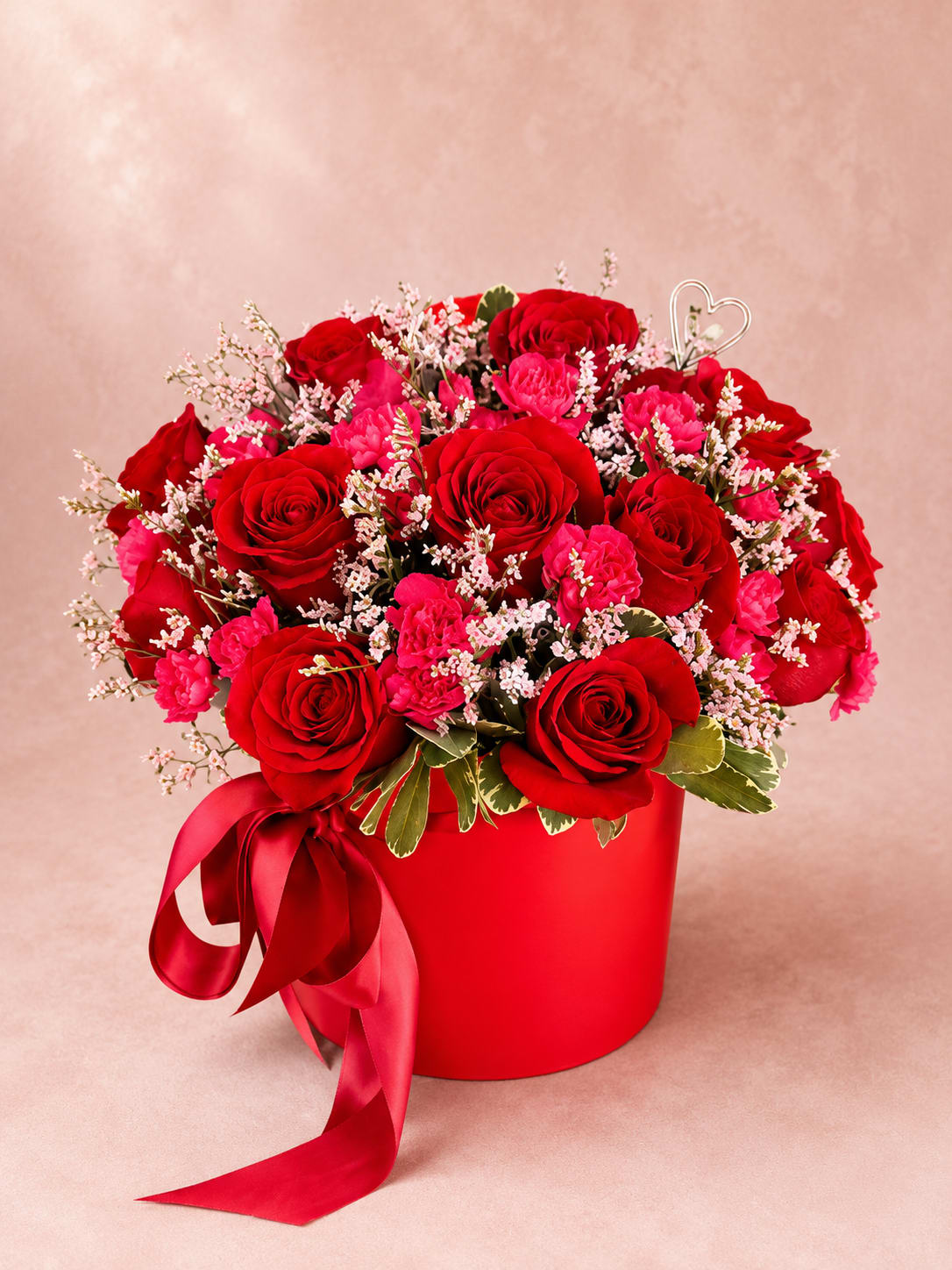 Sif's Ruby Sonata – Luxury Hat Box - Inspired by Sif, the Norse goddess of beauty, devotion, and enduring love, this elegant arrangement is a celebration of romance expressed through color, texture, and artistry.  Sif's Ruby Sonata brings together luxurious red roses, vibrant carnations, delicate pink limonium, and fresh seasonal greenery in a sophisticated hat box. Rich ruby tones are balanced with soft textures to create a composition that is both bold and graceful, like a beautifully composed sonata.  Perfect for anniversaries, Valentine's Day, birthdays, romantic surprises, or any occasion when you want to express heartfelt love and admiration with a truly memorable gift.  Every arrangement is handcrafted by Flower Fairy using the freshest premium flowers available. Seasonal substitutions may occasionally be necessary while preserving the overall style, color palette, and luxurious presentation.  Features: Premium red roses Vibrant carnations Delicate pink limonium Fresh seasonal greenery Luxury hat box Satin ribbon finish Handcrafted by Flower Fairy Same-day flower delivery throughout the Phoenix Metro Area