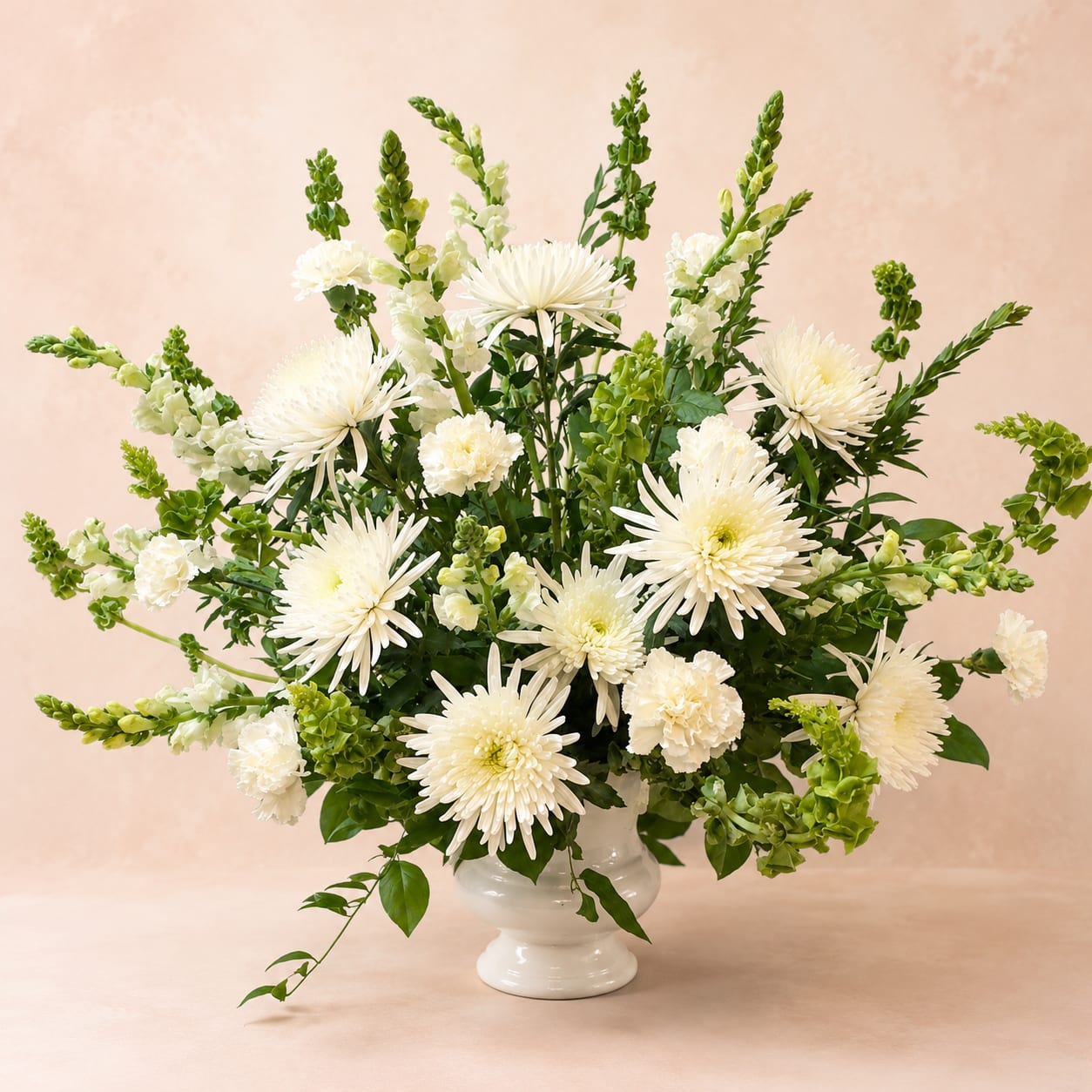 Galatea's Eternal Grace – Funeral Tribute Arrangement - Inspired by Galatea, whose story symbolizes beauty, hope, and enduring love, this elegant funeral tribute offers a heartfelt expression of remembrance and compassion.  Galatea's Eternal Grace is handcrafted with premium white spider chrysanthemums, graceful white snapdragons, delicate white carnations, and lush seasonal greenery. Designed in a classic memorial style, this elegant arrangement creates a peaceful presence at funeral services, memorial ceremonies, or celebrations of life.  The all-white palette symbolizes purity, peace, remembrance, and everlasting love, offering comfort to family and friends while honoring the memory of someone deeply cherished.  Each tribute is handcrafted by Flower Fairy using the freshest premium flowers available. While seasonal substitutions may occasionally be necessary, the overall white palette, elegant style, and heartfelt presentation will always be preserved.  Features: Premium white spider chrysanthemums White snapdragons White carnations Fresh seasonal greenery Designed in a durable funeral service urn Suitable for funeral services, memorials, and celebration of life ceremonies Handcrafted by Flower Fairy Same-day delivery to funeral homes, churches, cemeteries, and memorial venues throughout the Phoenix Metro Area