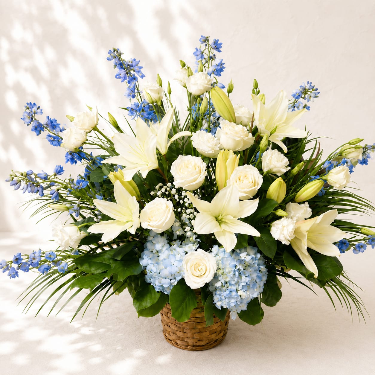 Aura's Heavenly Grace – Sympathy Basket - Inspired by Aura, the gentle Greek Titaness of the morning breeze, this elegant sympathy basket symbolizes peace, hope, and the quiet comfort of cherished memories.  Aura's Heavenly Grace is handcrafted with fresh white Asiatic lilies, premium white roses, soft blue hydrangeas, graceful blue delphinium, delicate white lisianthus, miniature carnations, baby's breath, and lush seasonal greenery. Beautifully arranged in a woven basket, its serene white and blue palette reflects purity, peace, and everlasting remembrance.  Thoughtfully designed to offer comfort during funeral services, memorial ceremonies, and celebrations of life, this elegant floral tribute expresses sincere sympathy while honoring a loved one with dignity and grace.  Each arrangement is handcrafted by Flower Fairy using the freshest premium flowers available. Seasonal substitutions may occasionally be necessary while preserving the overall color palette, style, and value of the design.  Features: White Asiatic lilies Premium white roses Blue hydrangeas Blue delphinium White lisianthus White miniature carnations Baby's breath Fresh seasonal greenery Woven sympathy basket Handcrafted by Flower Fairy Appropriate for funeral services, memorials, and celebrations of life Same-day delivery to funeral homes, churches, cemeteries, and memorial venues throughout the Phoenix Metro Area