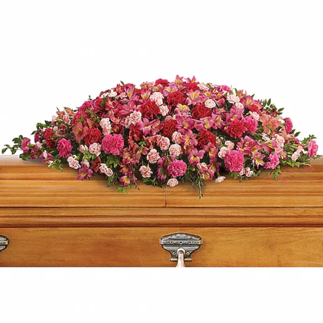 Pink and red floral casket spray on a wooden casket