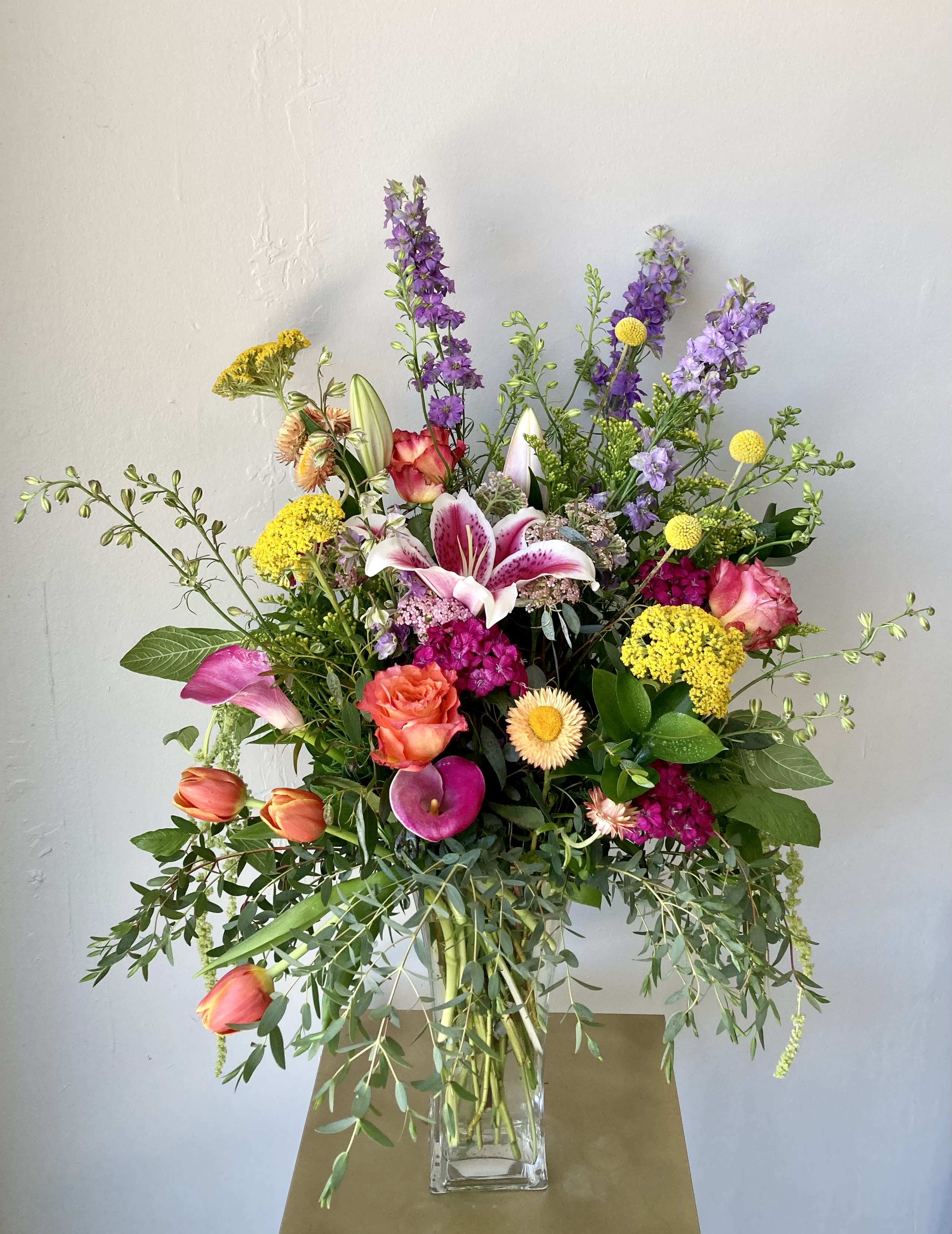 Mixed bouquet with lilies, roses, tulips, and purple spikes in a glass vase