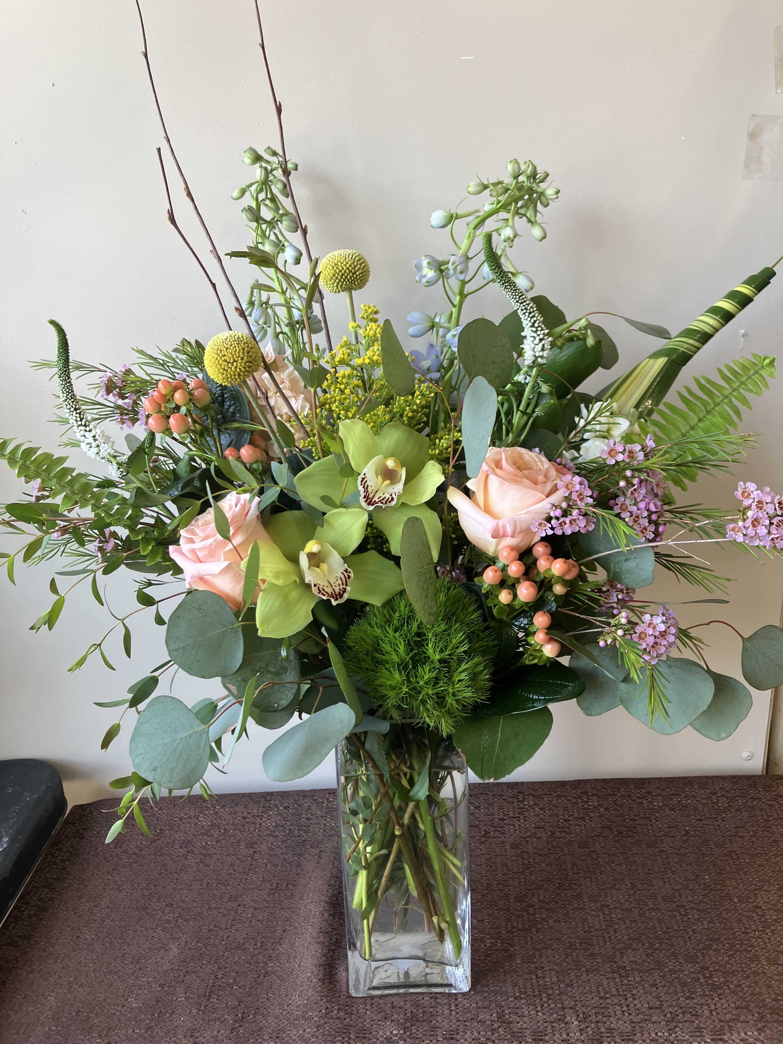 Tall mixed bouquet in a clear glass vase with roses and orchids