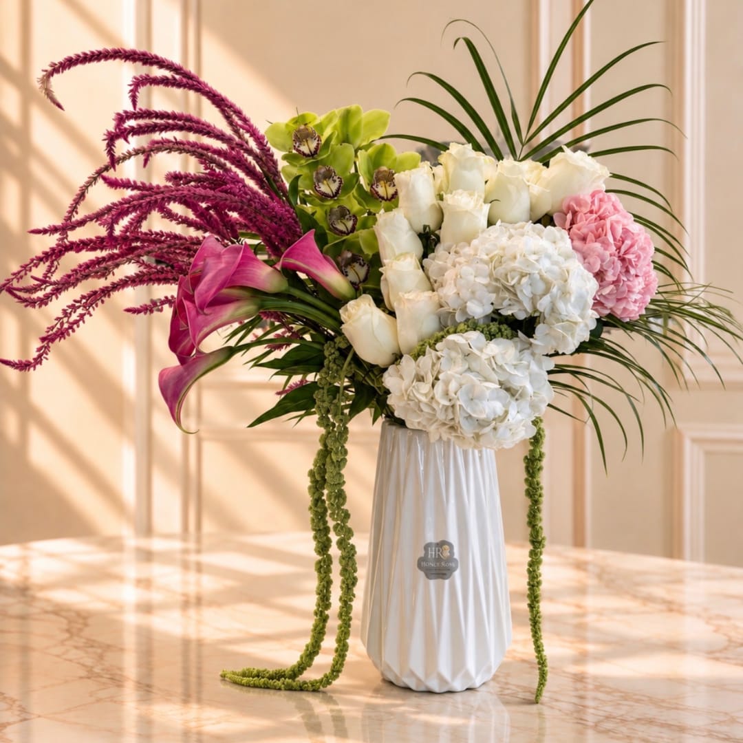Tall floral arrangement with white roses, hydrangeas, pink calla lilies, and purple amaranthus in a white vase