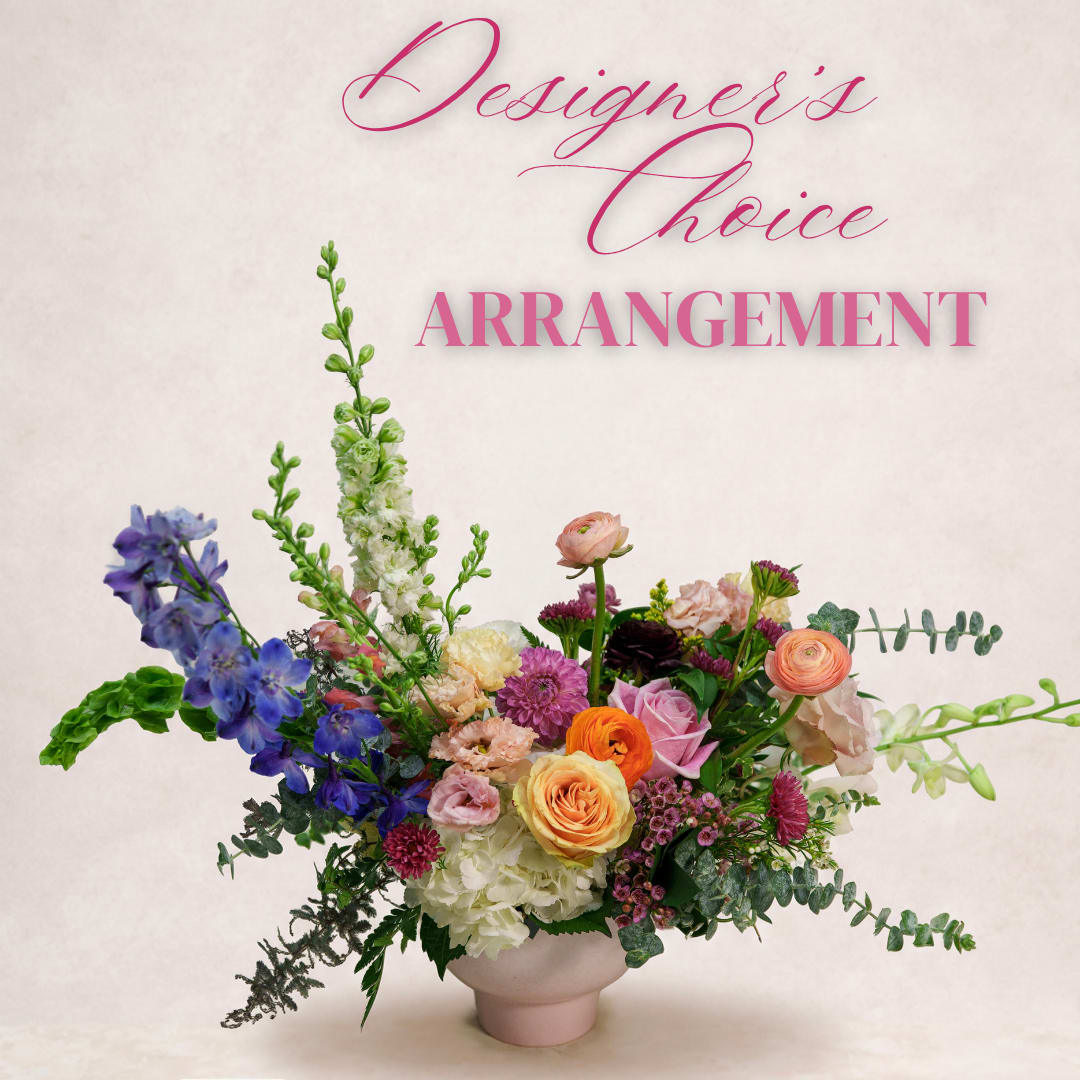 Colorful mixed flower arrangement in a pale vase with tall blue blooms