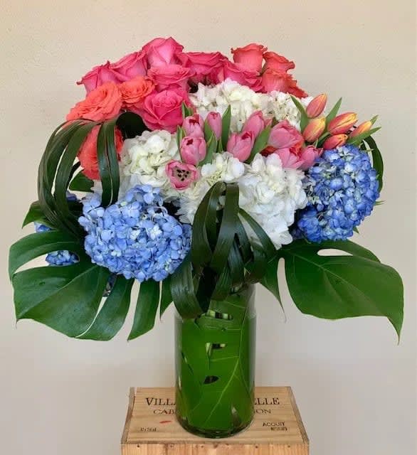 Bouquet of pink roses, tulips, white flowers, and blue hydrangeas in a green vase