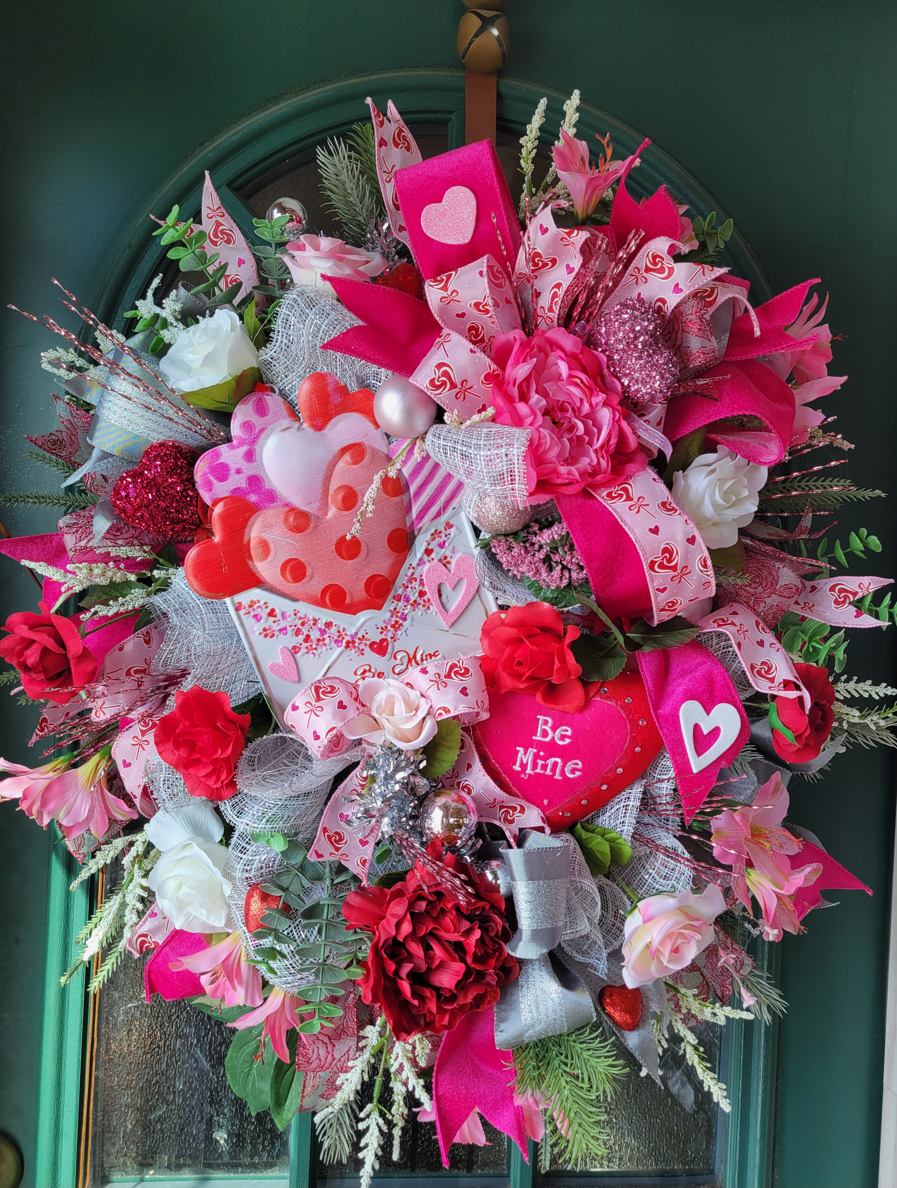 Heart-themed wreath with pink and red flowers, ribbons, and a "Be Mine" sign
