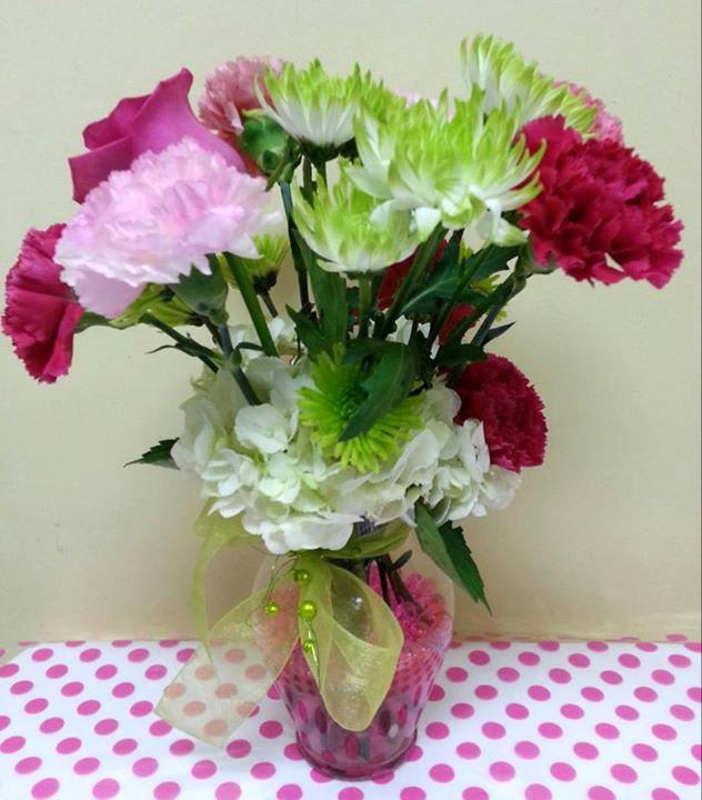 Pink, white, and green carnations in a glass vase with a ribbon