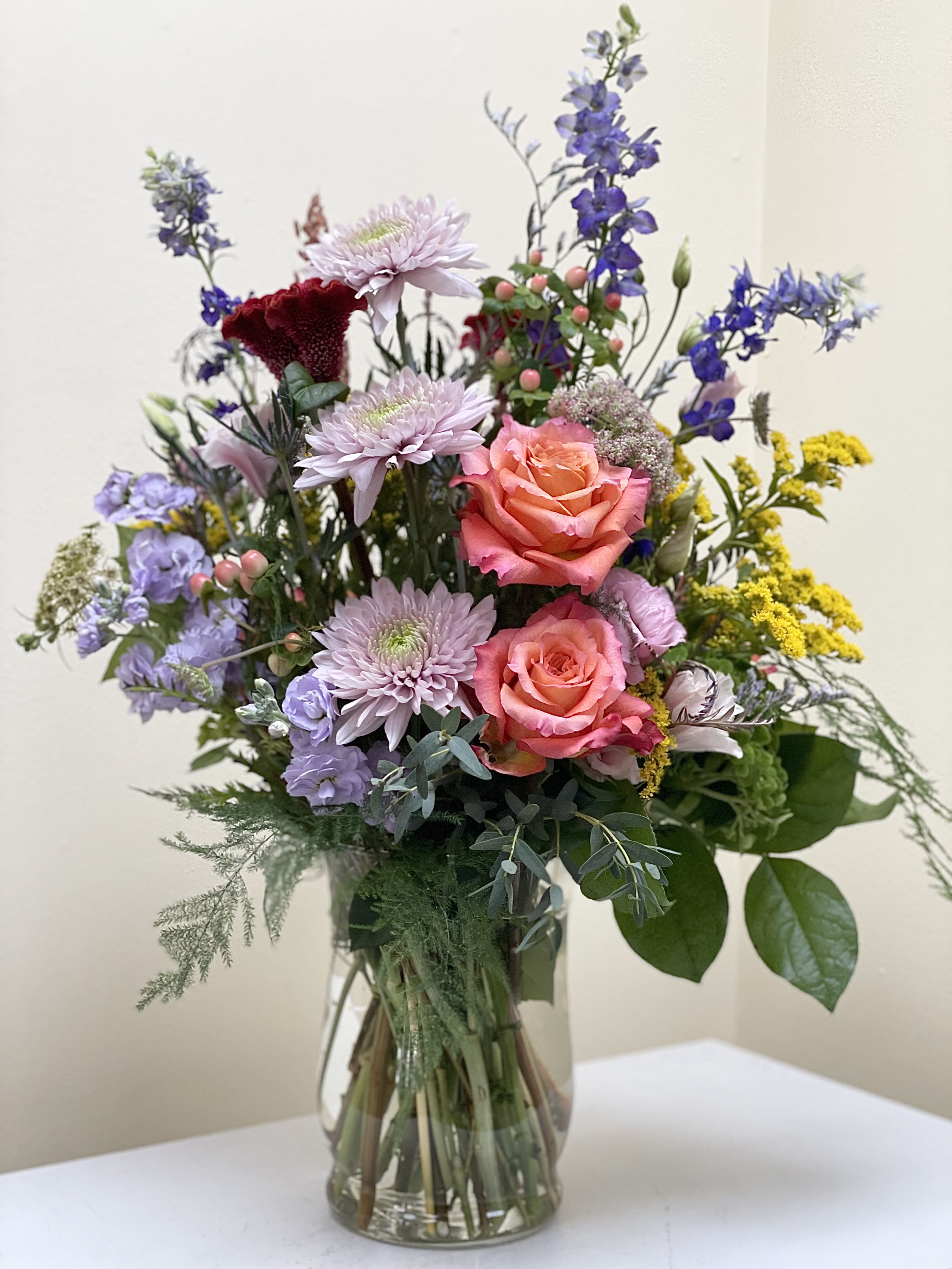 Mixed bouquet of pink roses, lavender blooms, and blue flowers in a glass vase